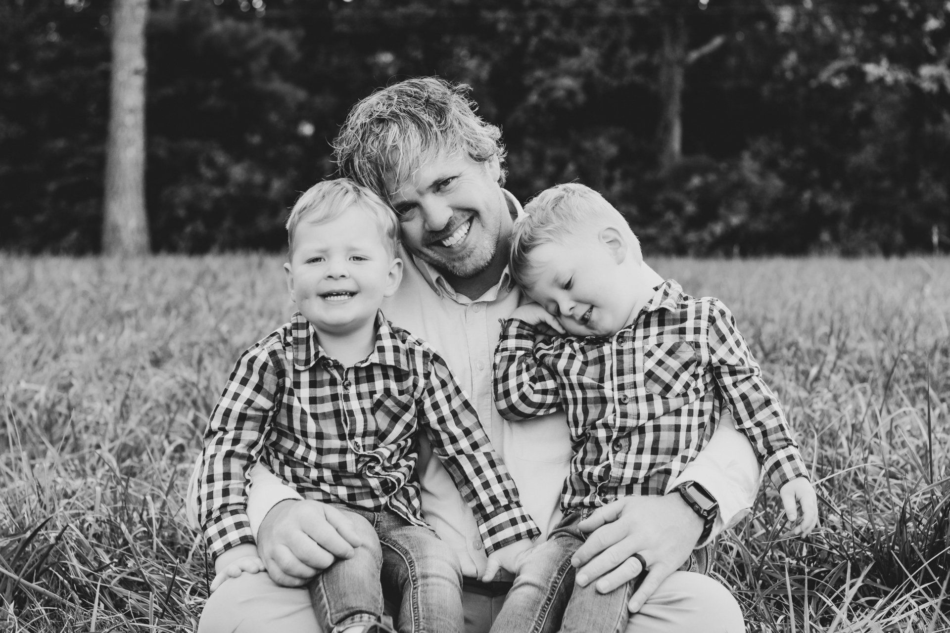 A man is sitting in the grass with two young boys.