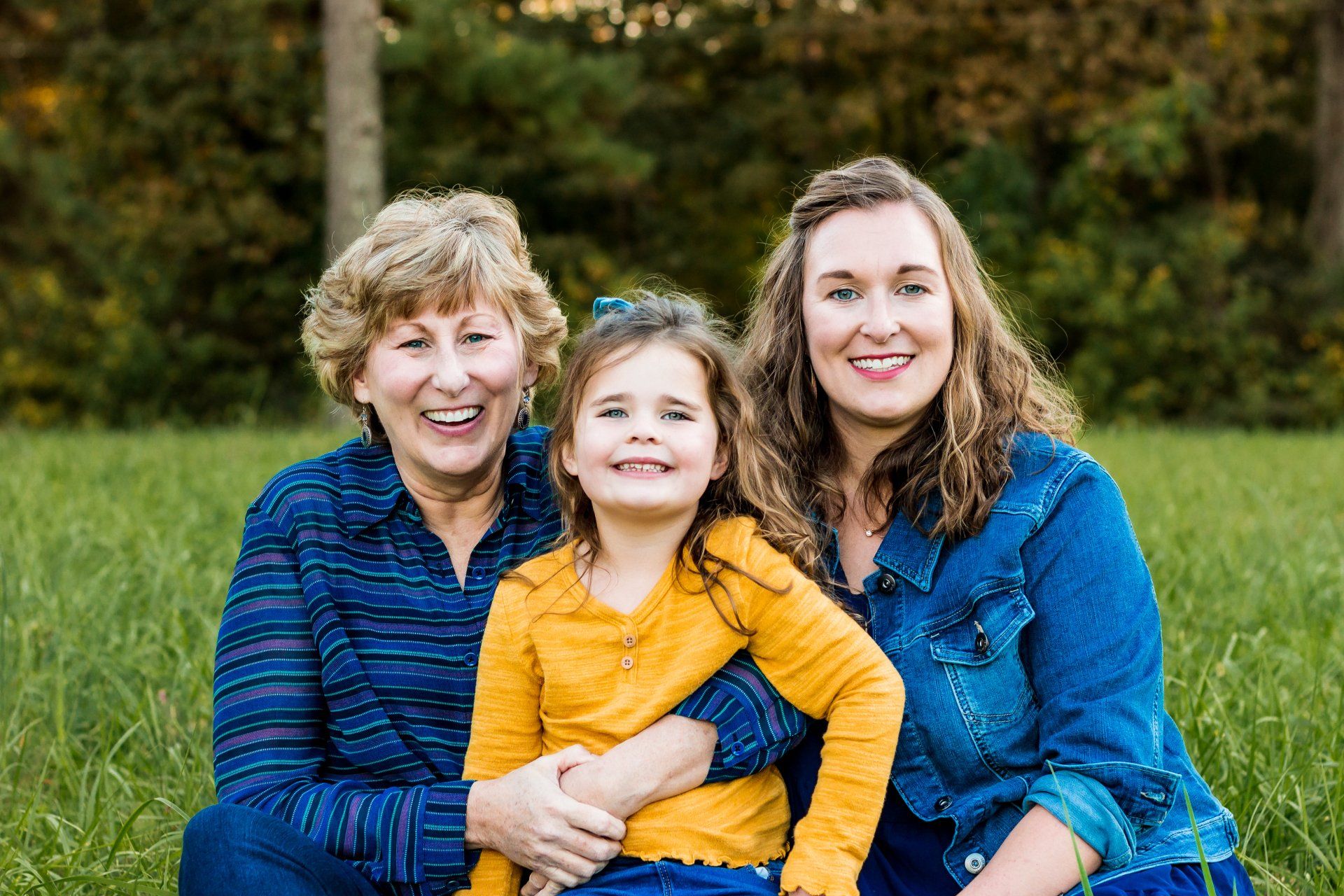 Three women are posing for a picture with a little girl in a field.