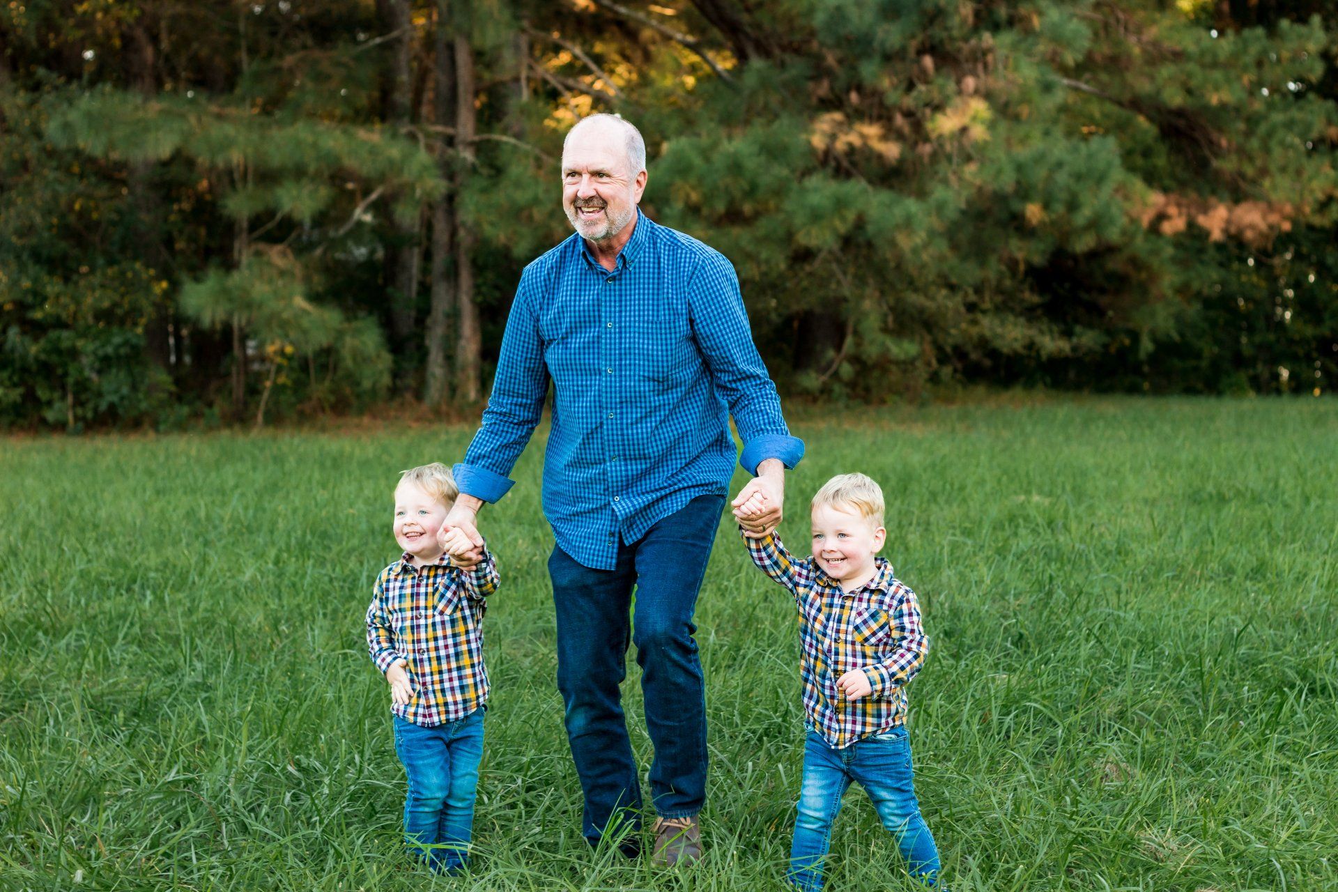 A man is holding hands with two young boys in a field.