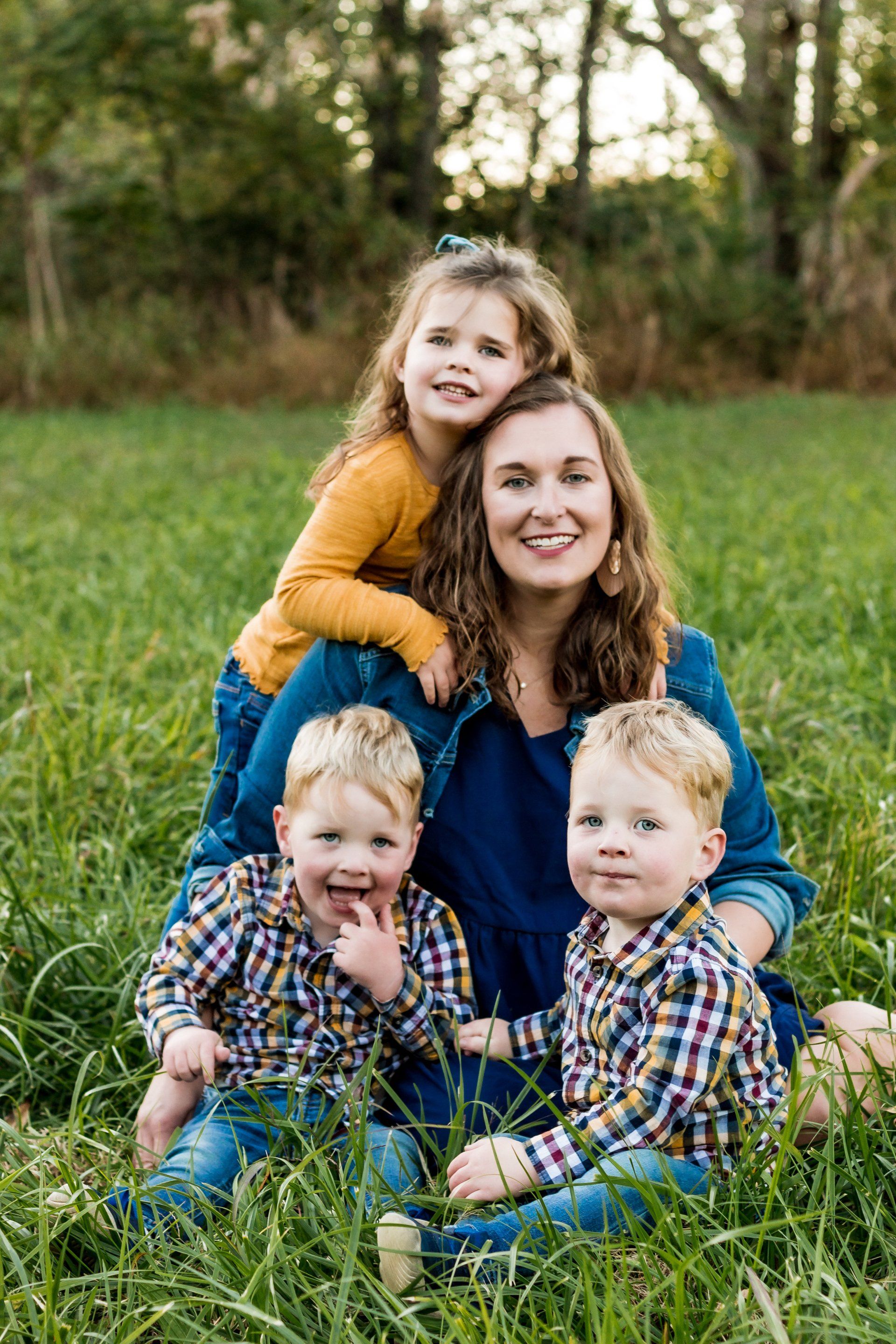 A woman is sitting in the grass with three children.