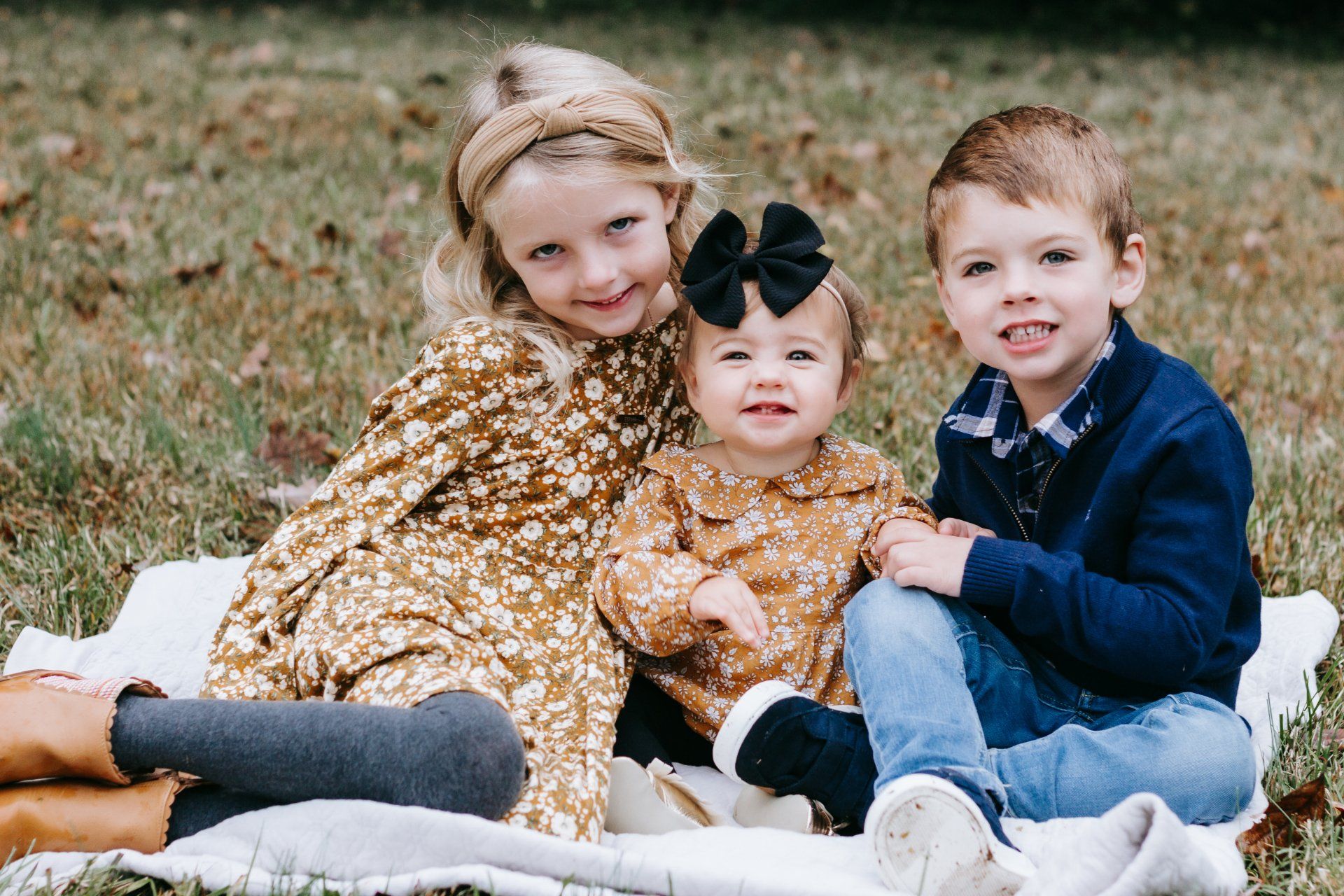 Three children are sitting on a blanket in the grass.