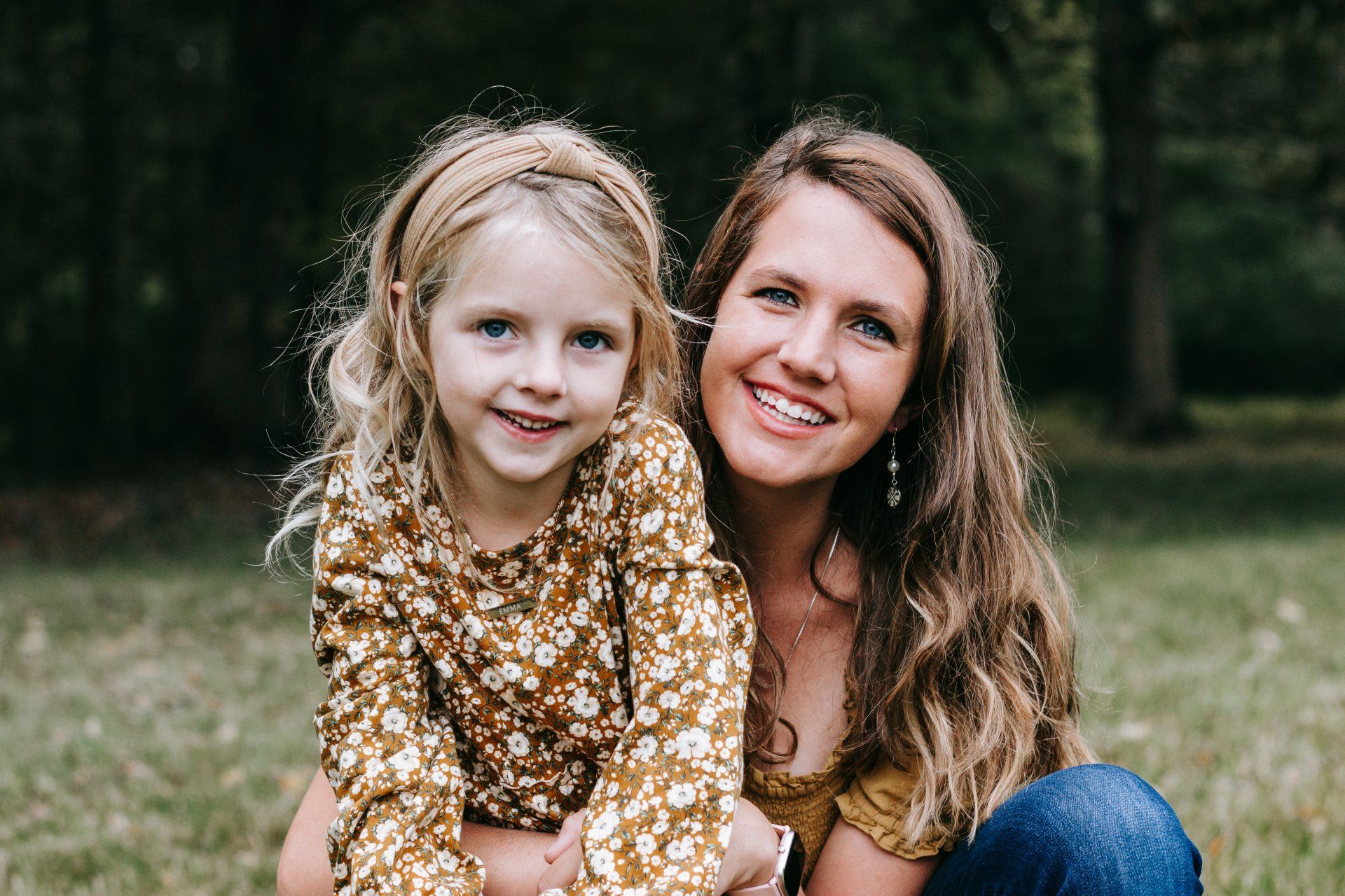 A woman and a little girl are posing for a picture in the grass.
