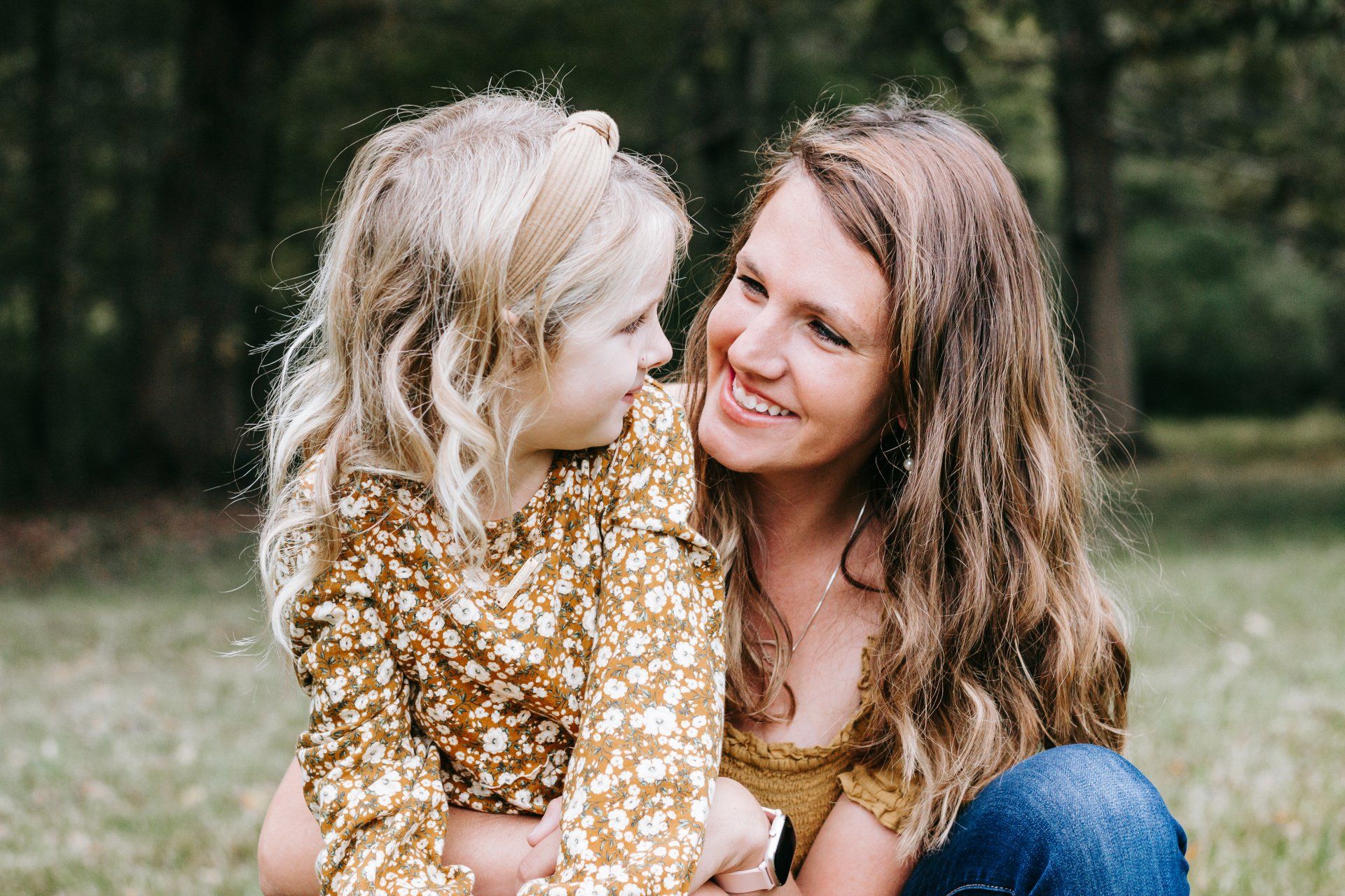 A woman and a little girl are sitting in the grass looking at each other.