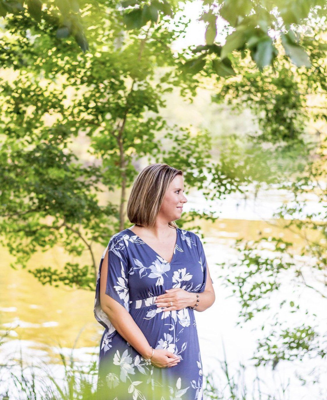 A woman in a blue dress is standing in front of a lake.