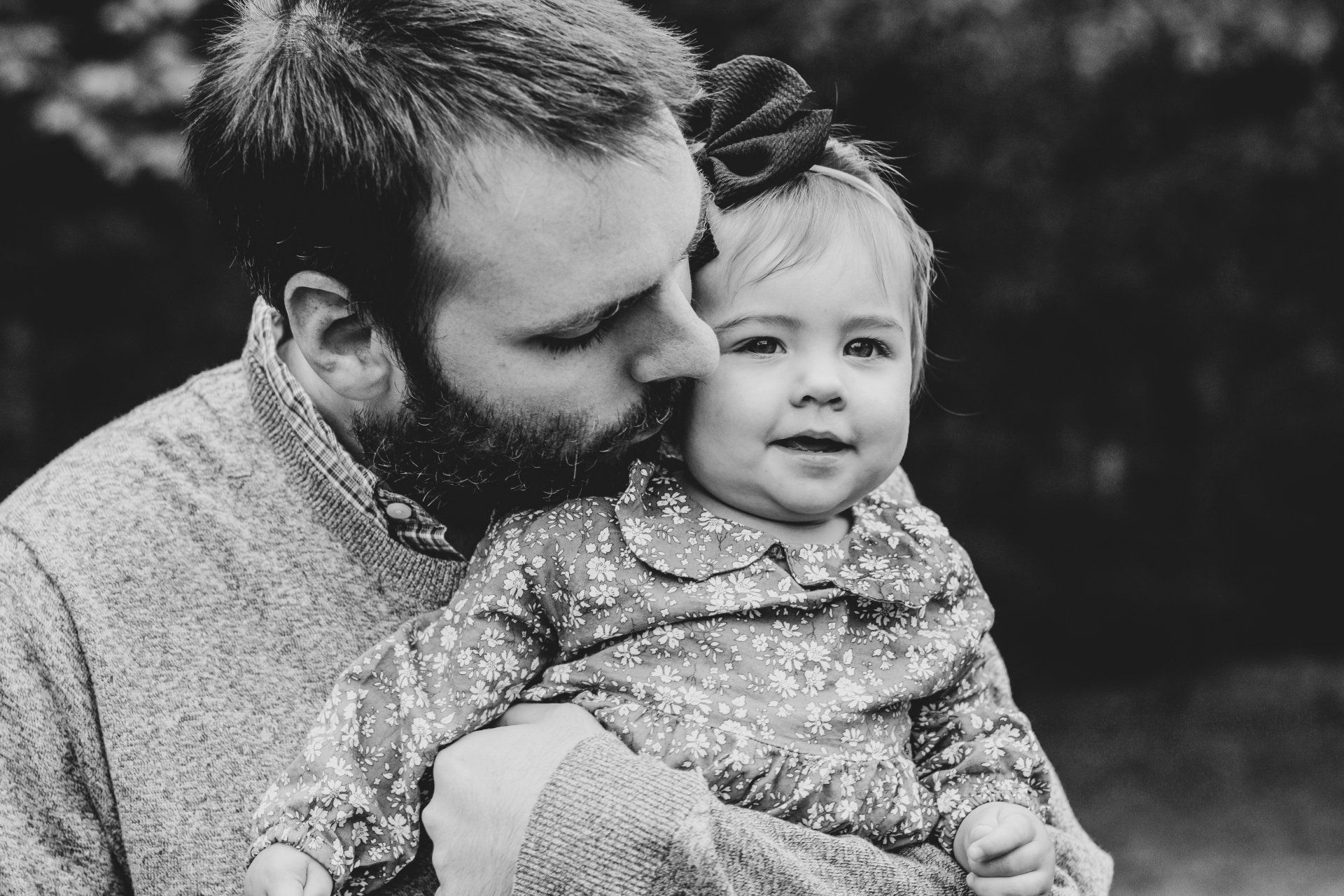 A man is holding a baby girl in his arms and kissing her on the cheek.