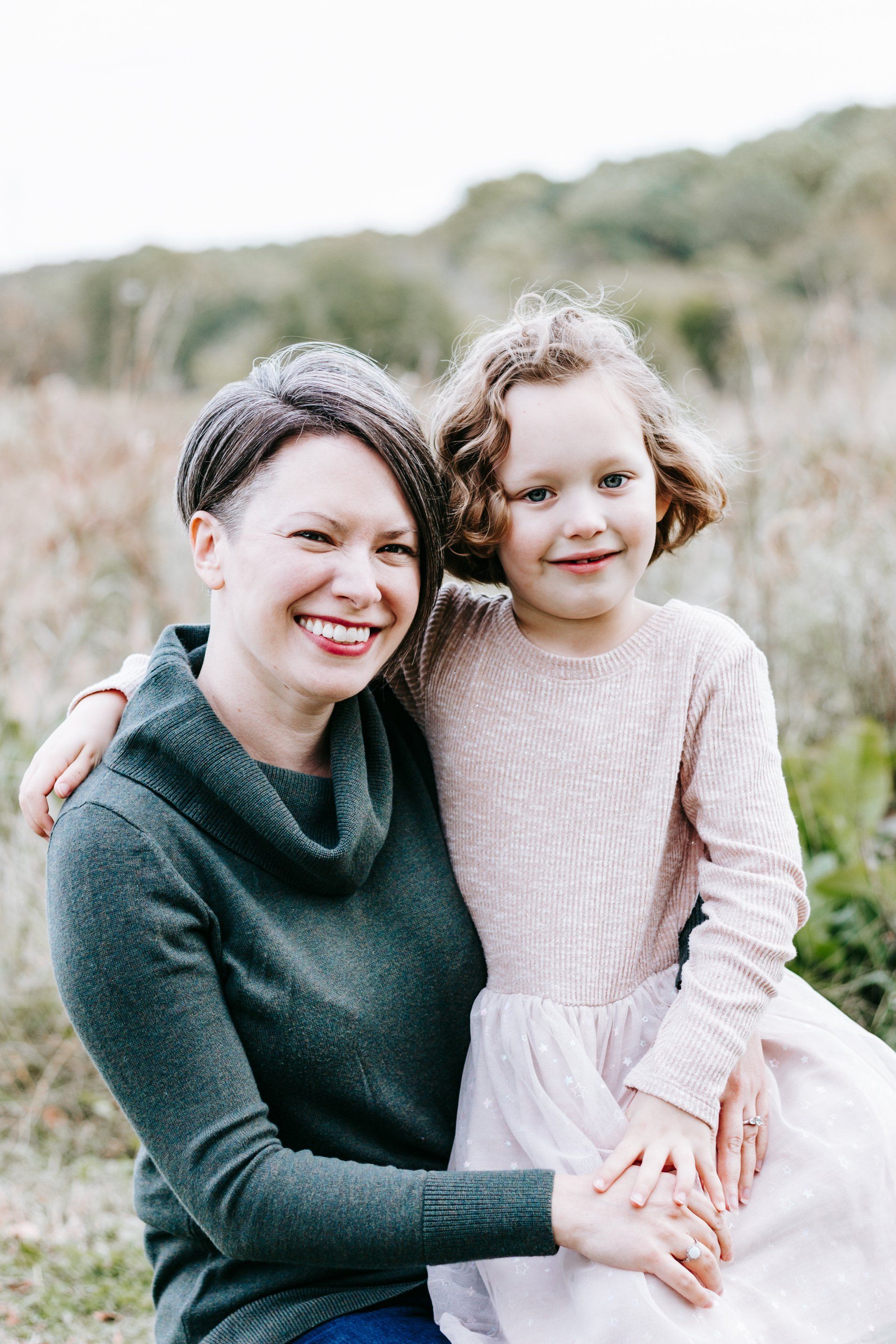 A woman and a little girl are sitting next to each other in a field.