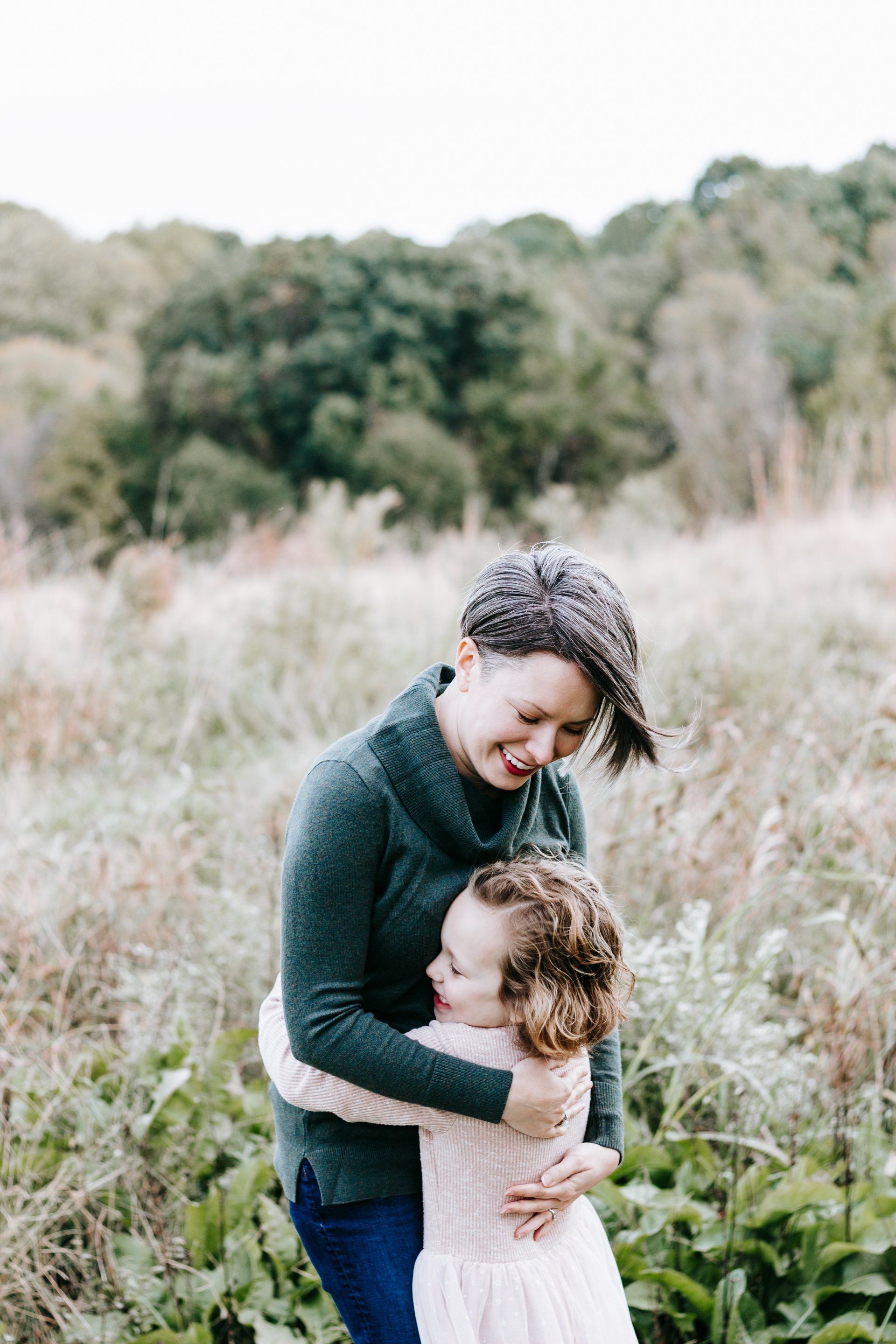 A woman is hugging a little girl in a field.