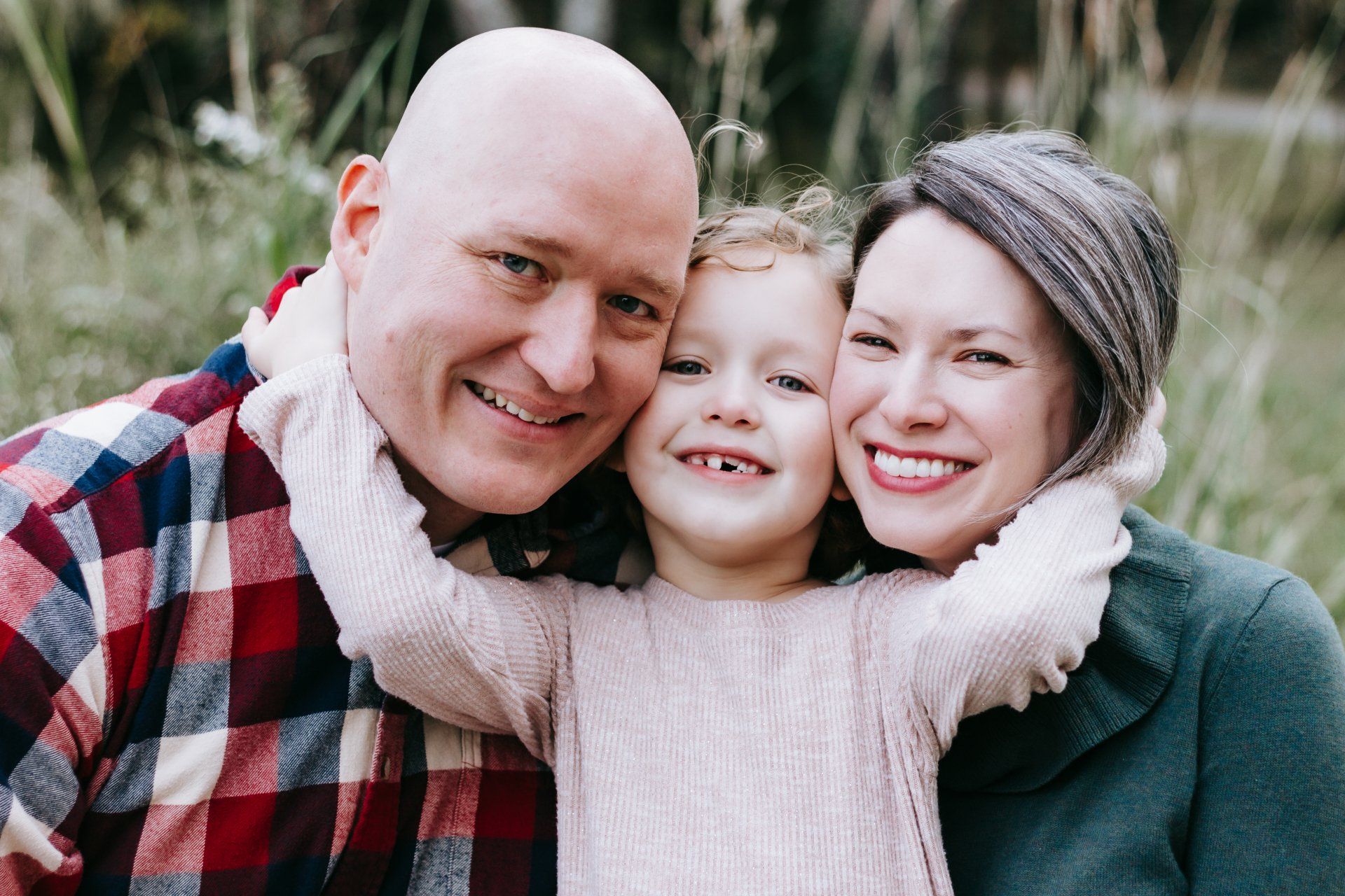 A man and woman are hugging a little girl and smiling for the camera.
