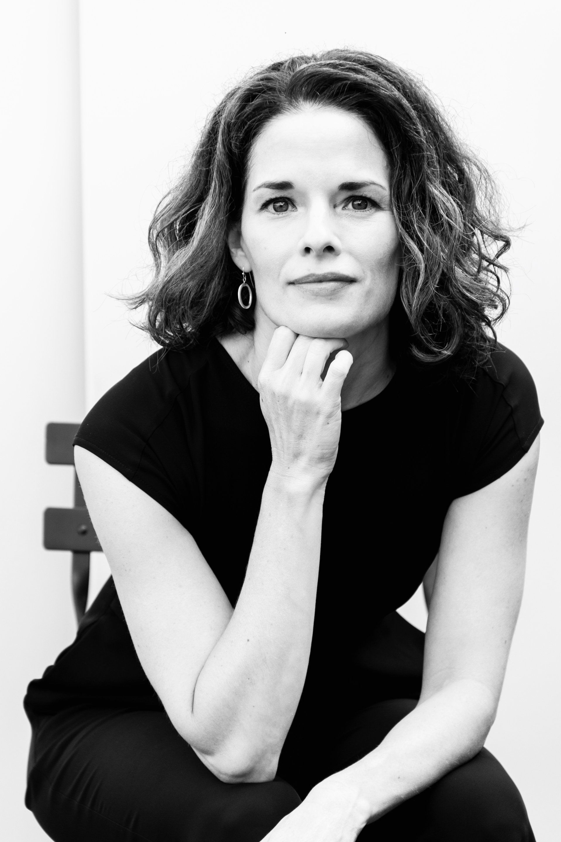 A black and white photo of a woman sitting with her hand on her chin.