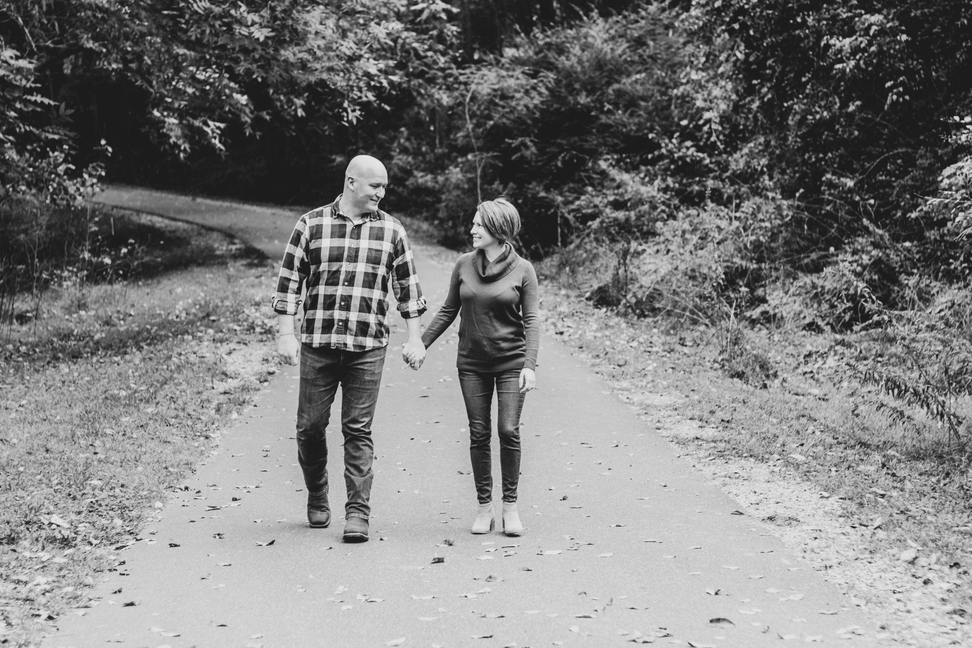 A man and a woman are walking down a dirt road holding hands.