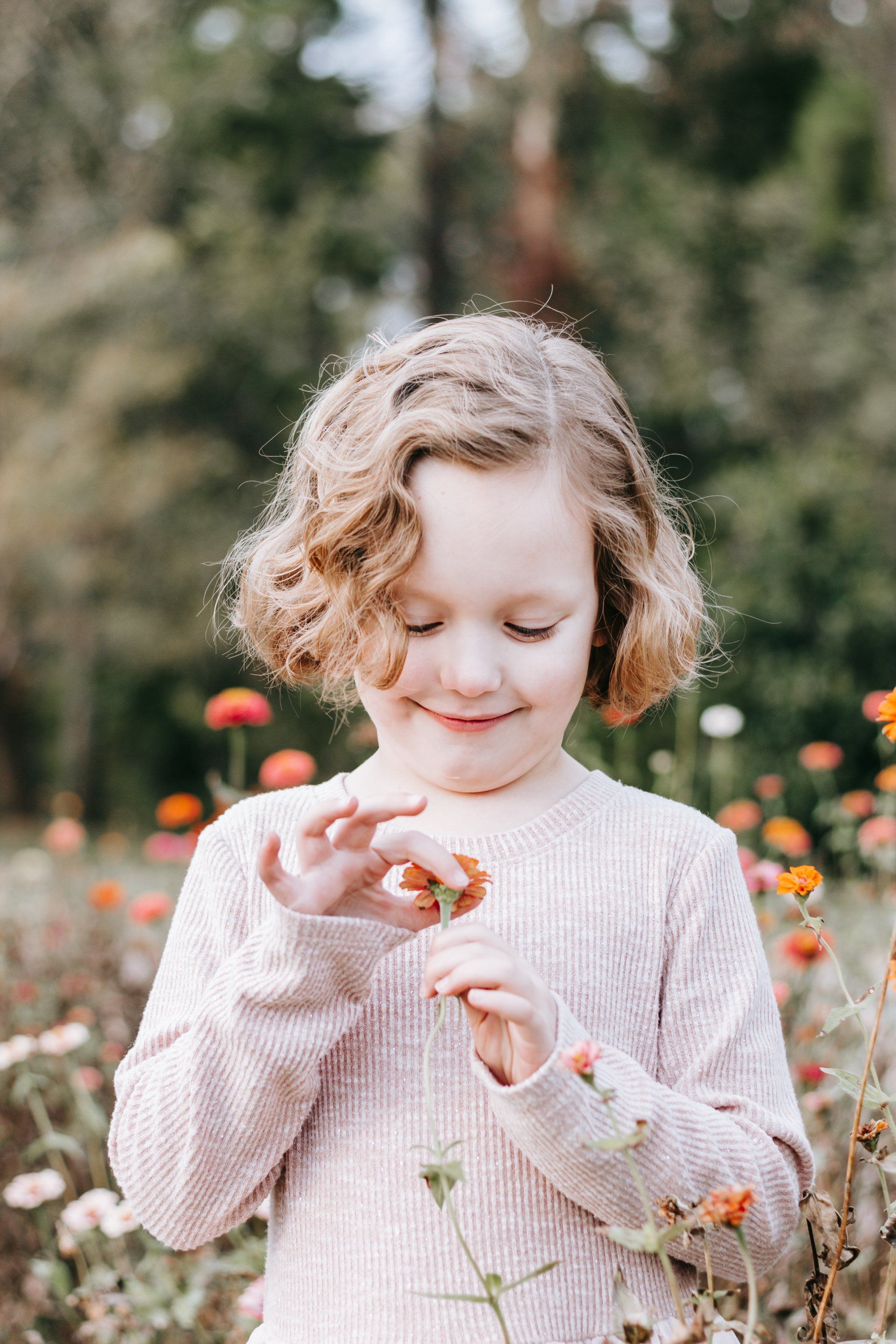 A little girl is standing in a field of flowers holding a flower.