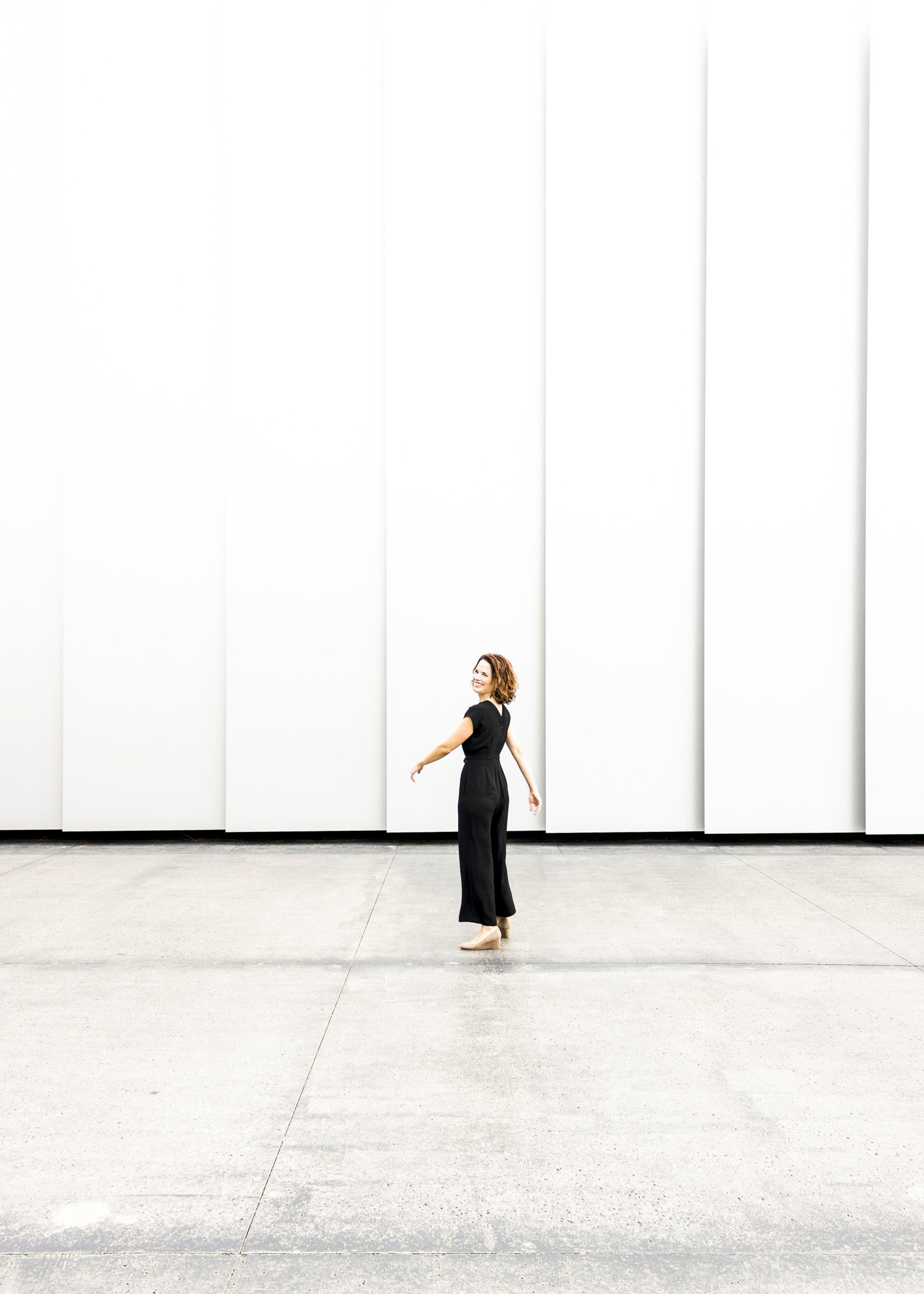 A woman in a black dress is standing in front of a white wall.