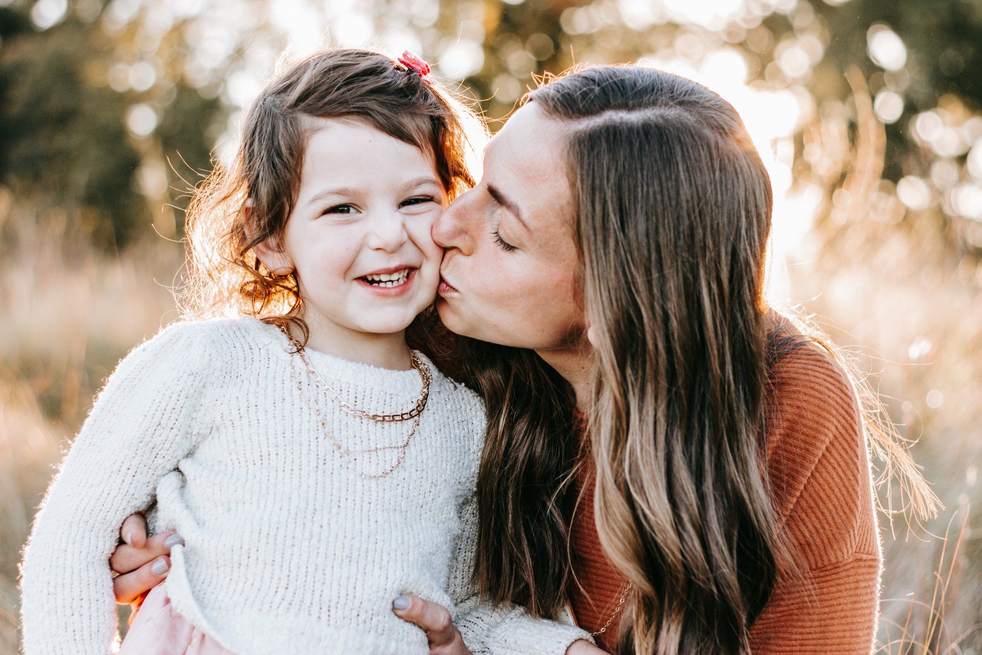 A woman is kissing her little girl on the cheek.