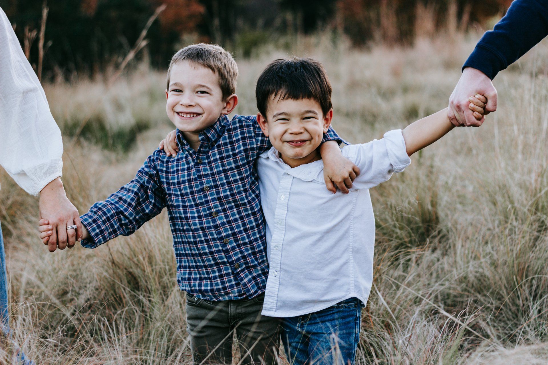 Two young boys are holding hands in a field with their parents.
