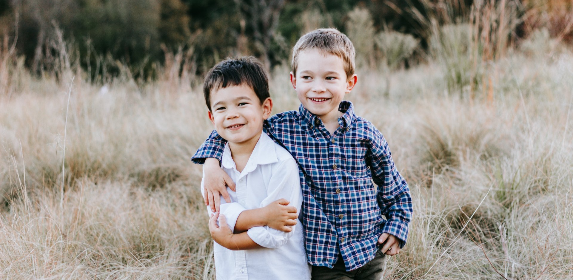 Two young boys are hugging each other in a field.