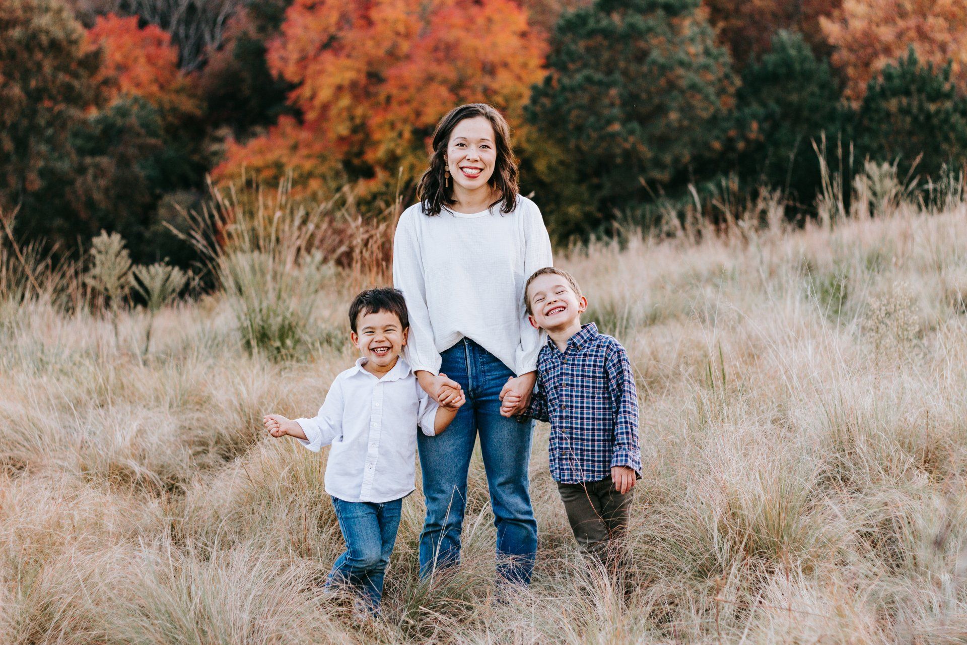 A woman and two children are standing in a field holding hands.
