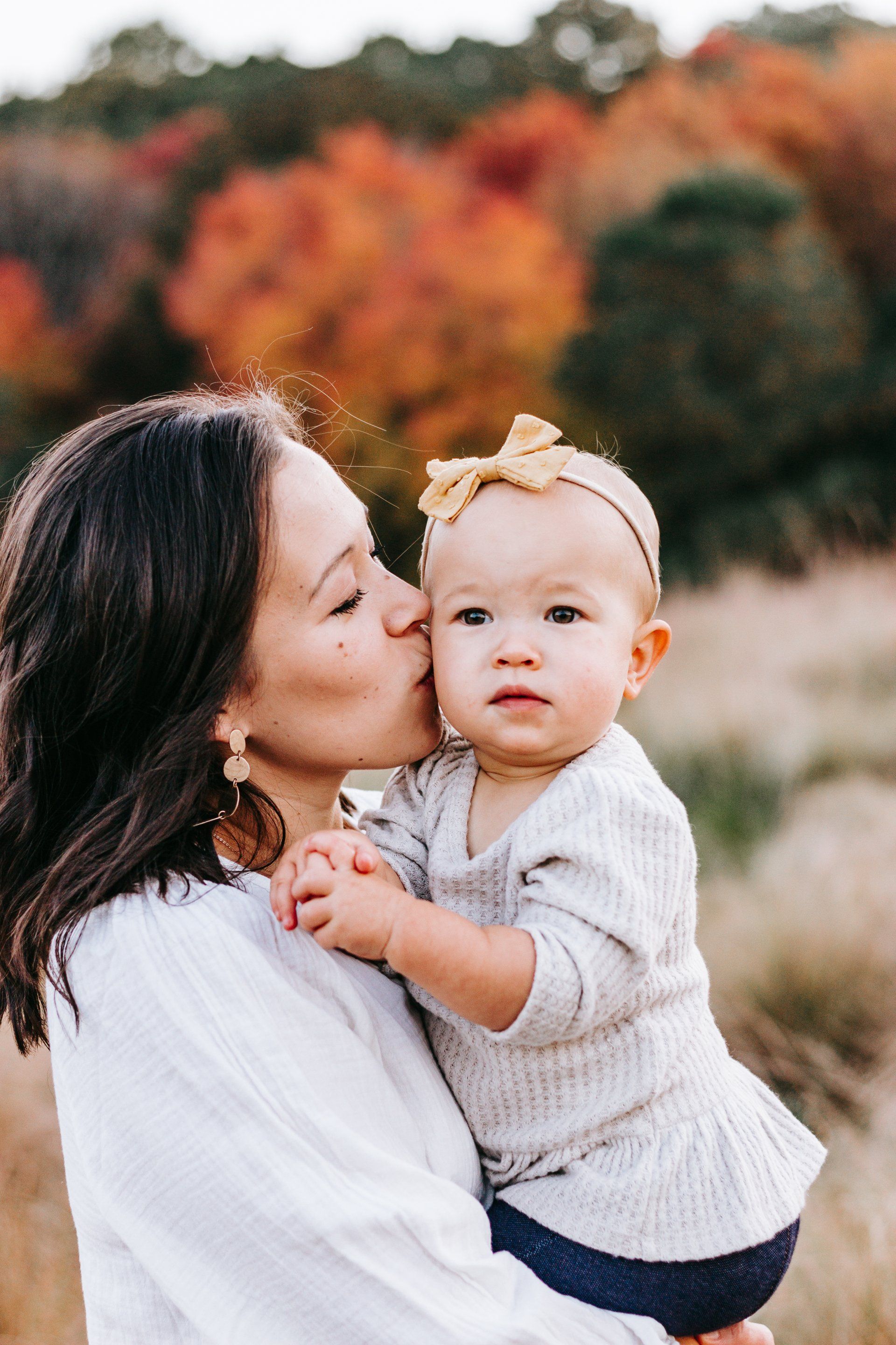 A woman is kissing a baby on the cheek in a field.
