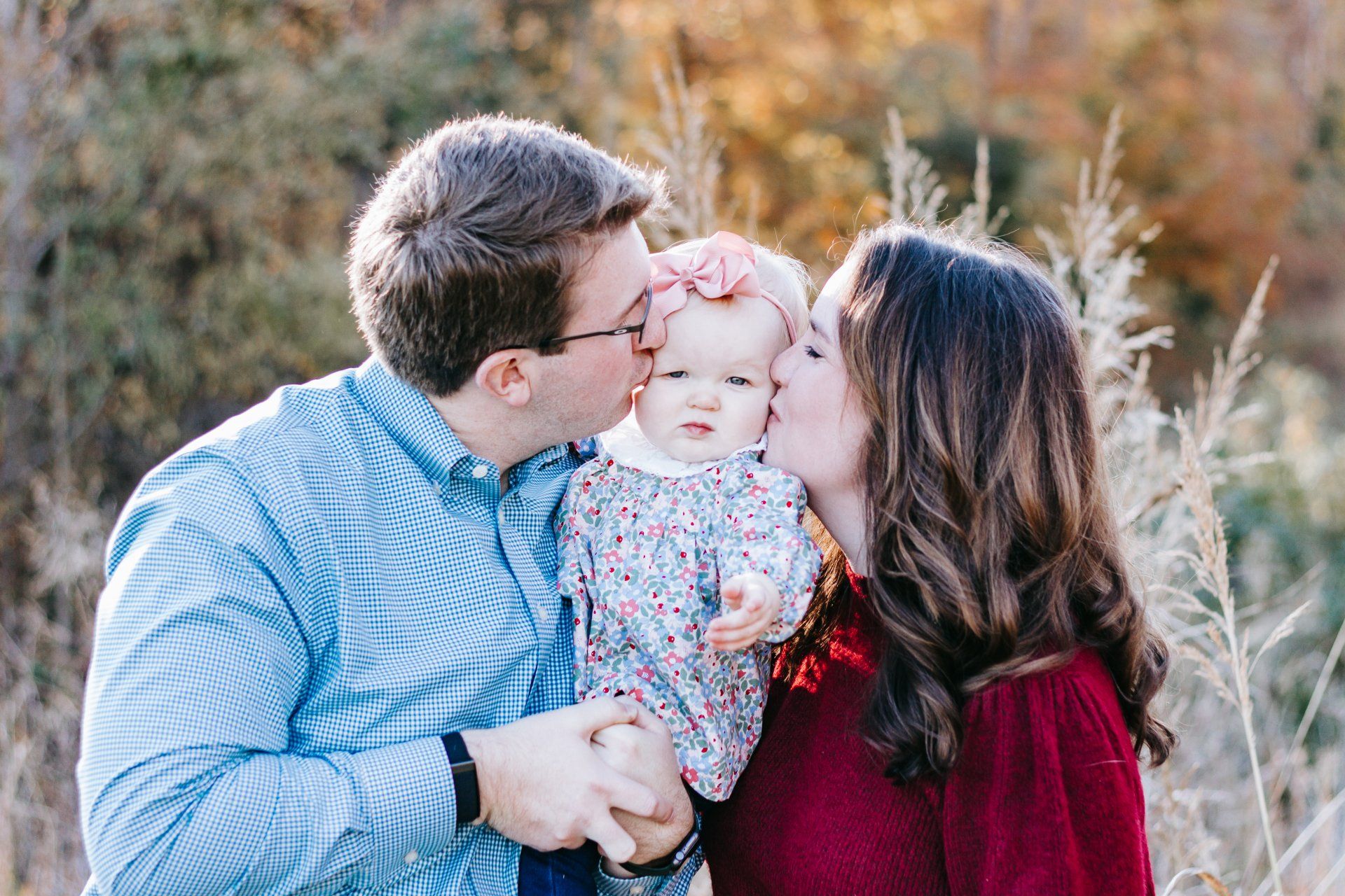 A man and woman are kissing a baby on the cheek.