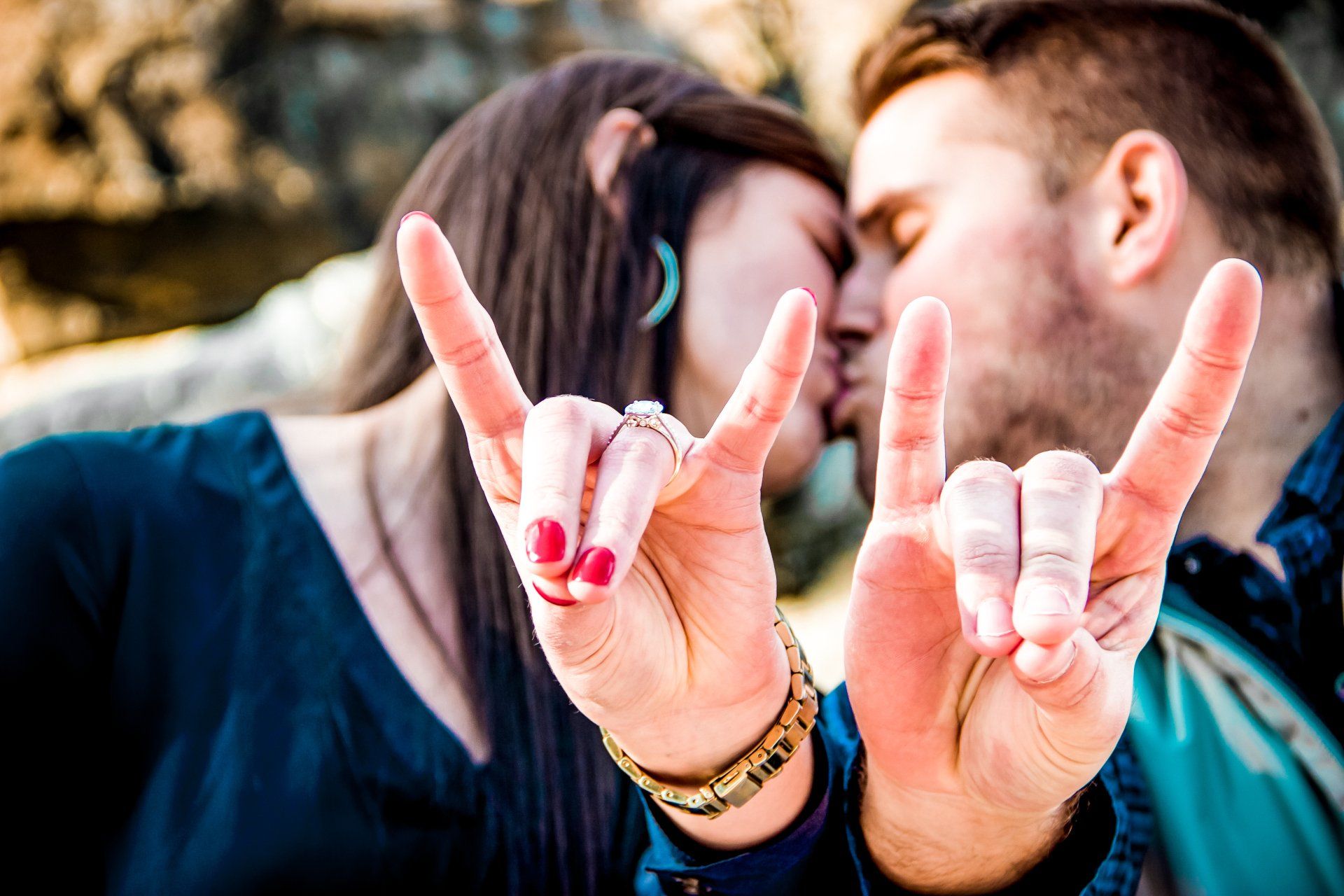 A man and a woman are kissing while making a peace sign with their hands.