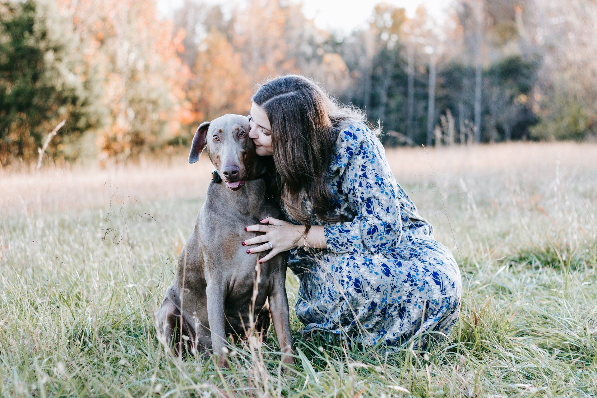A woman is kneeling down next to a dog in a field.