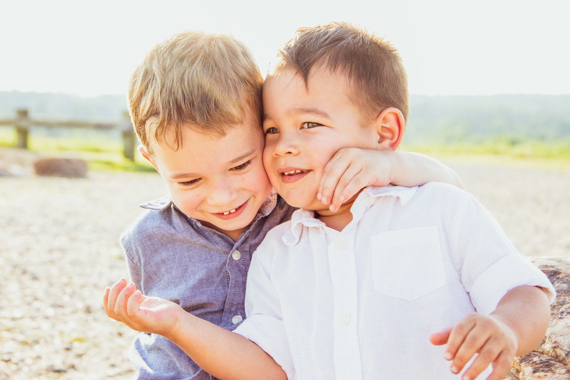 Two young boys are hugging each other on the beach.