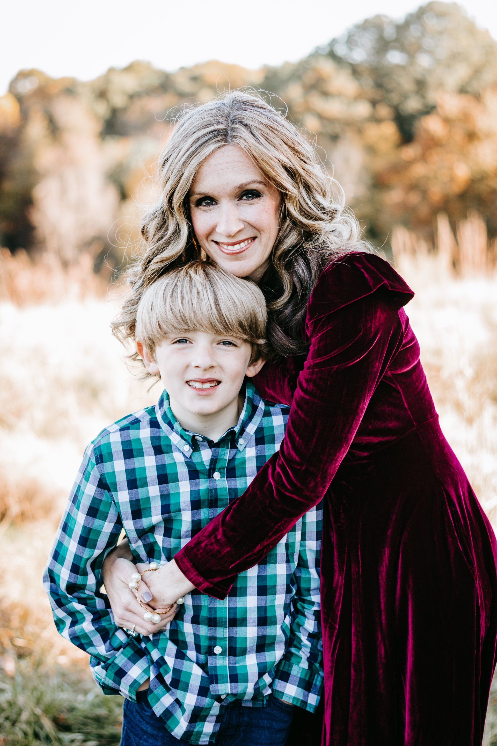 A woman in a red dress is hugging a young boy in a field.