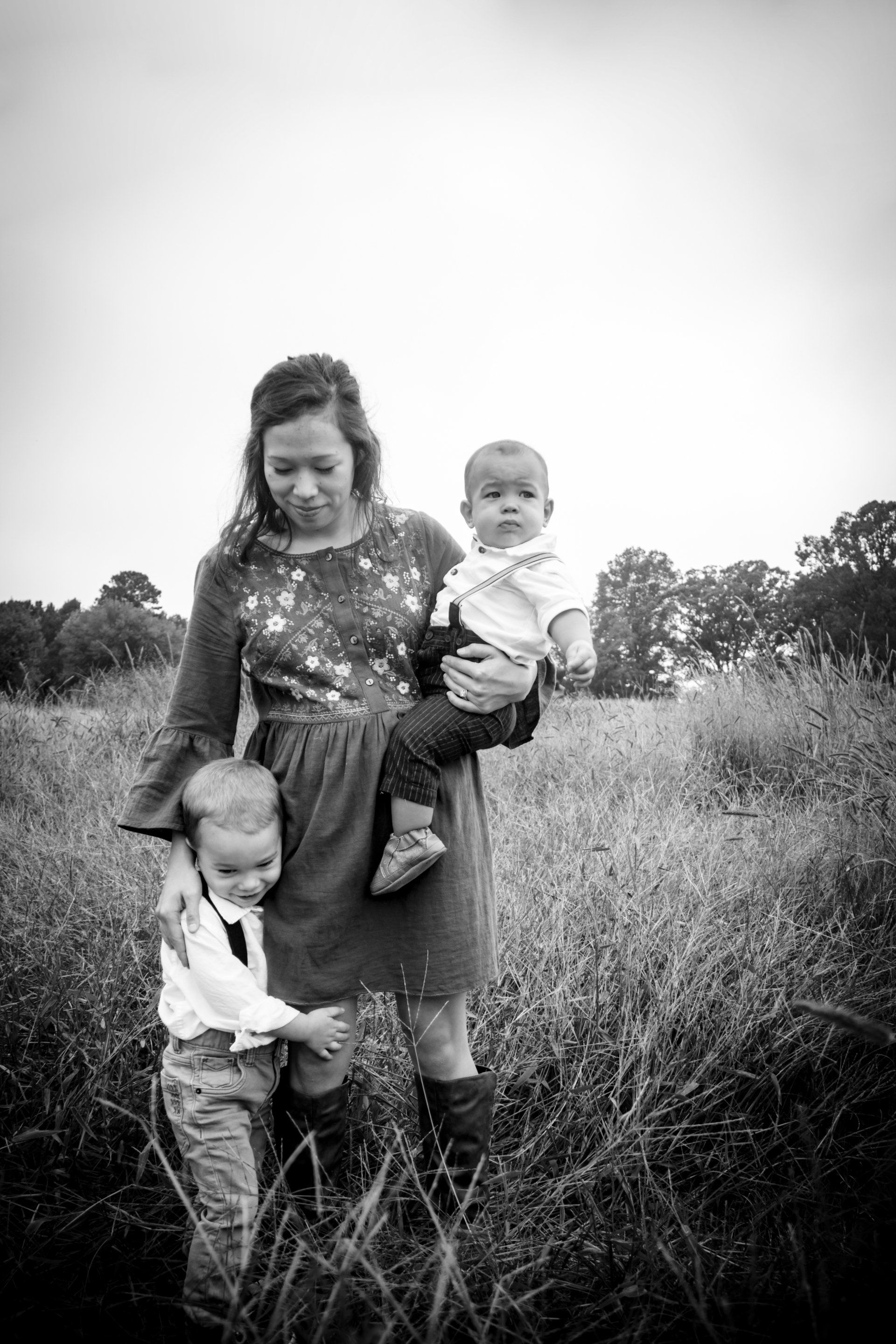 A woman is holding two children in a field in a black and white photo.