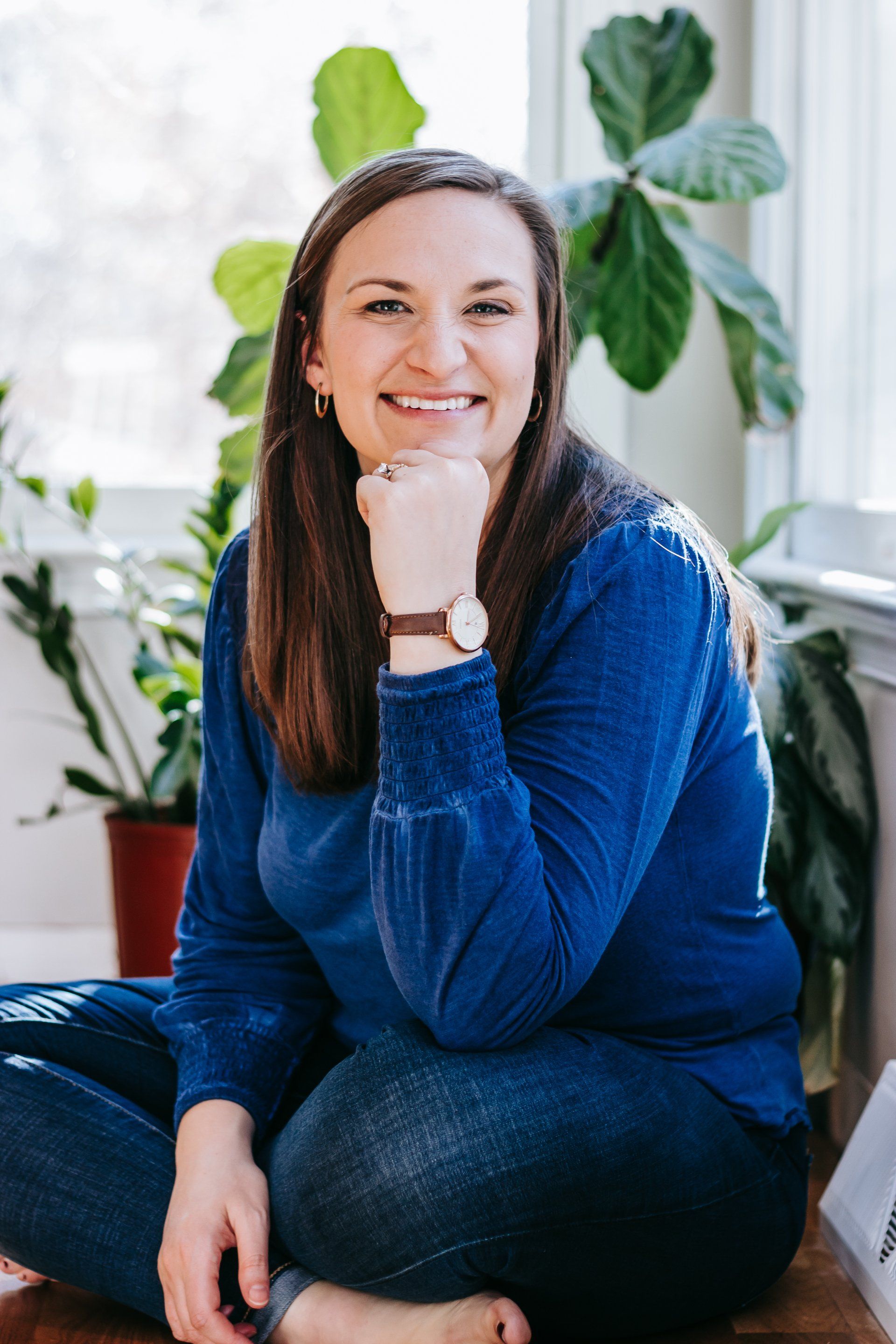A woman is sitting on the floor with her legs crossed and smiling.