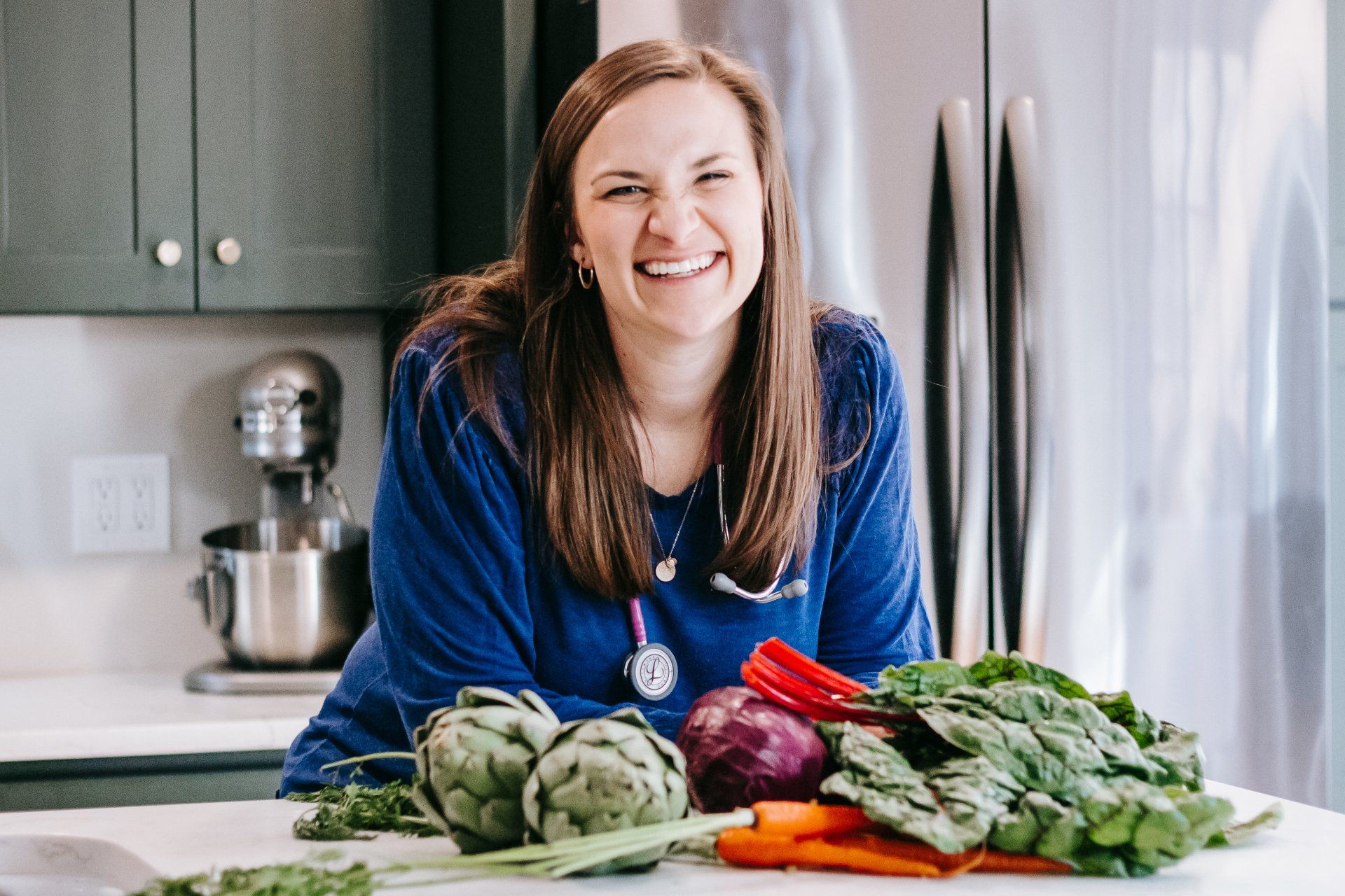 A woman is standing in a kitchen next to a table full of vegetables.