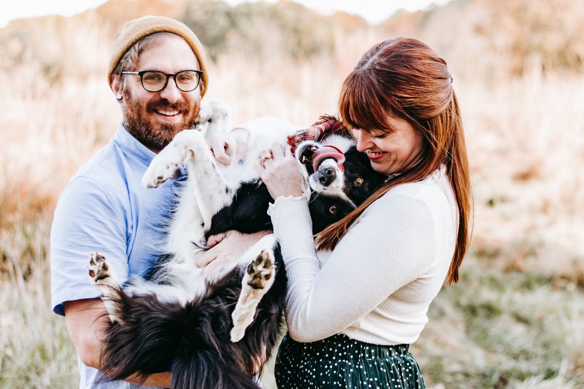 A man and a woman are holding a dog in a field.