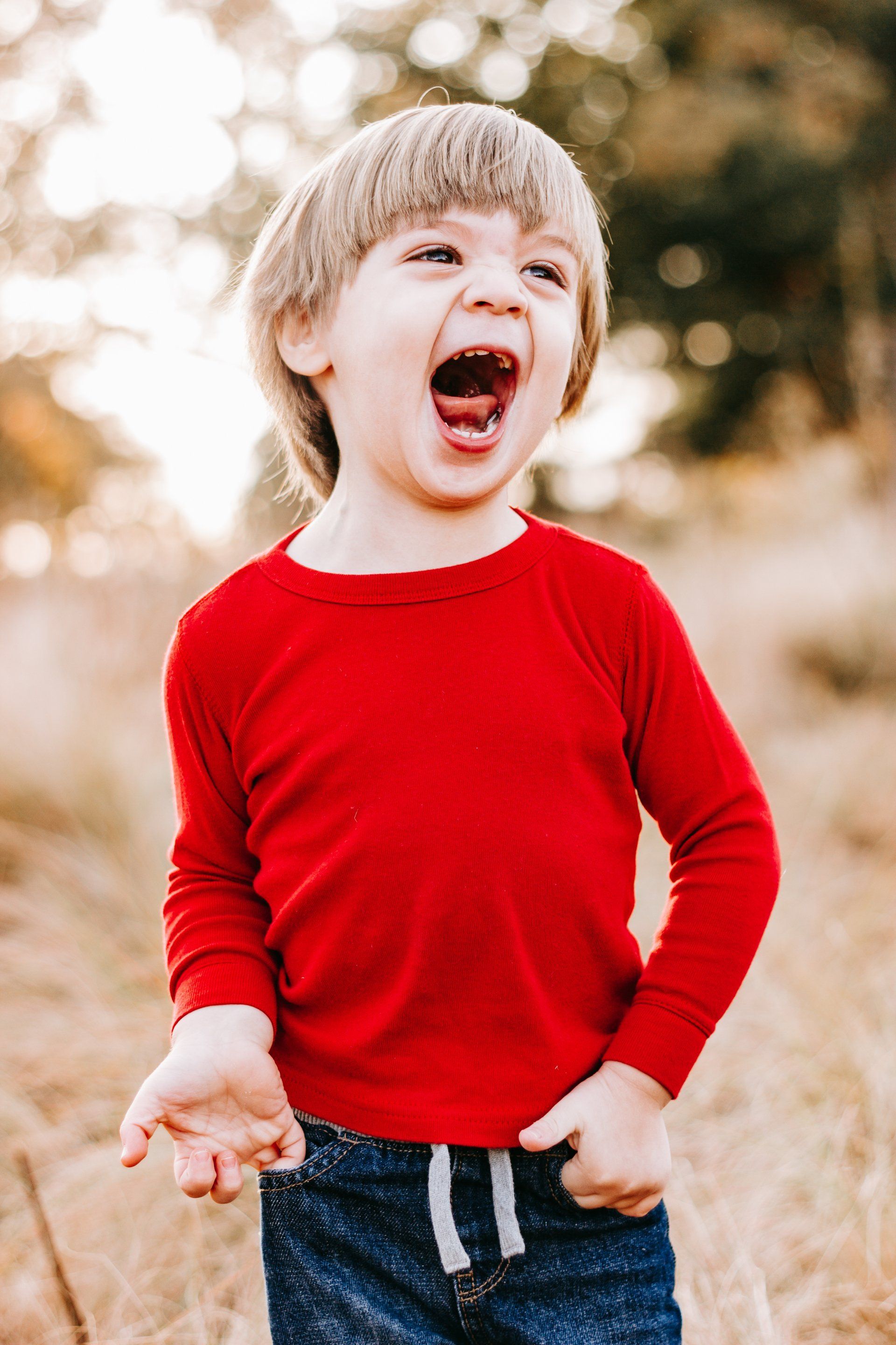 A little boy in a red shirt is laughing with his mouth open.