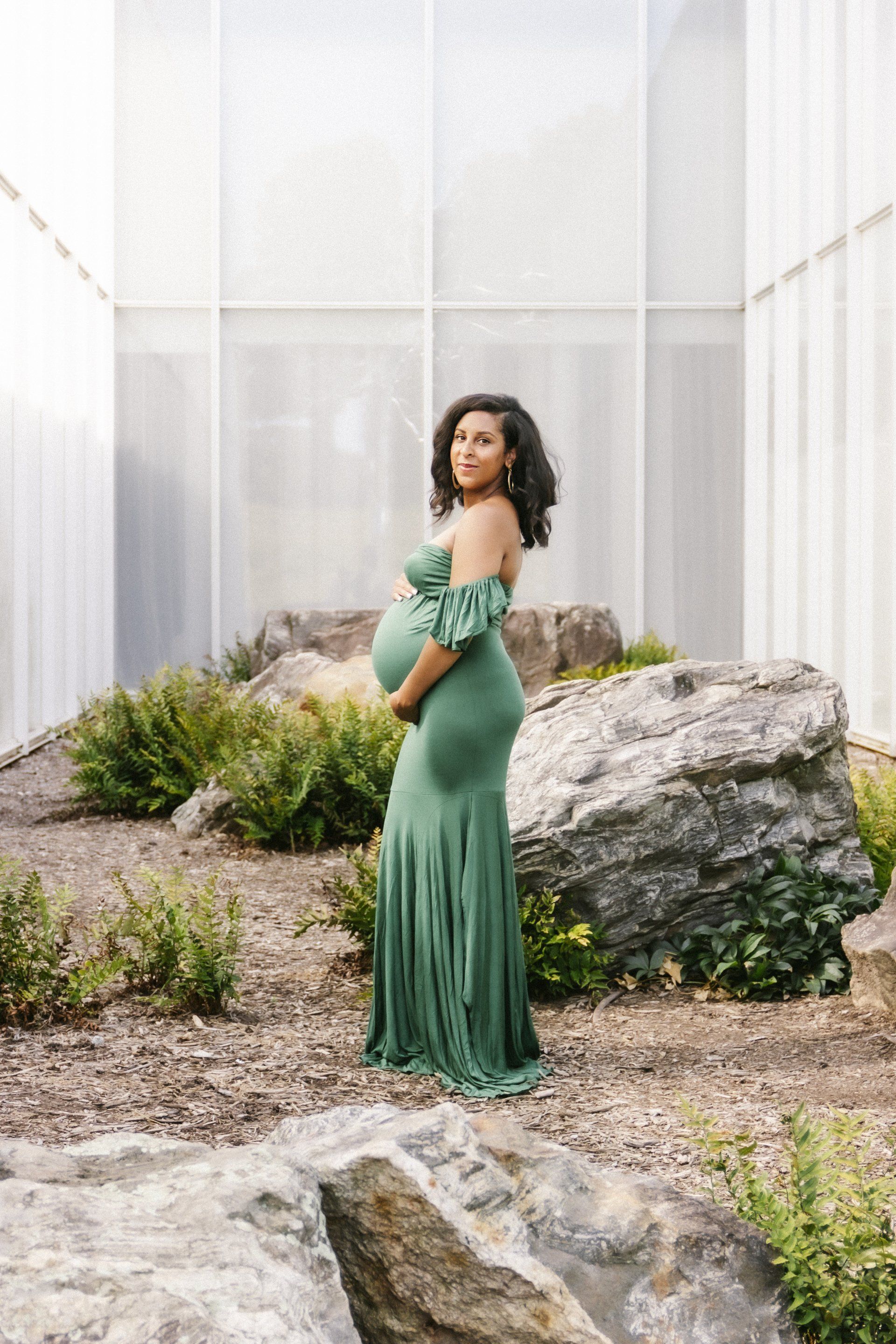 A pregnant woman in a green dress is standing in front of a building.