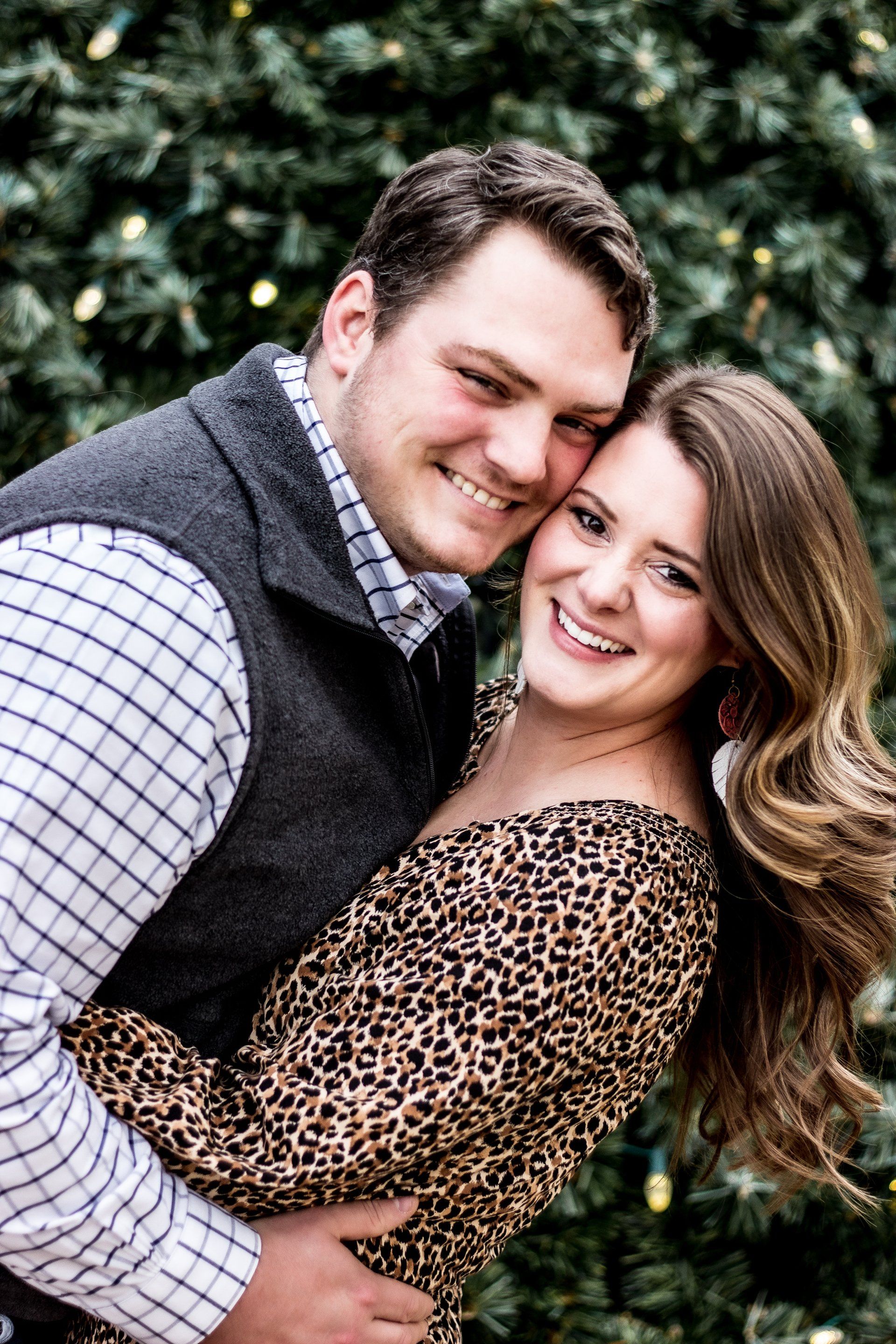 A man and a woman are posing for a picture in front of a christmas tree.