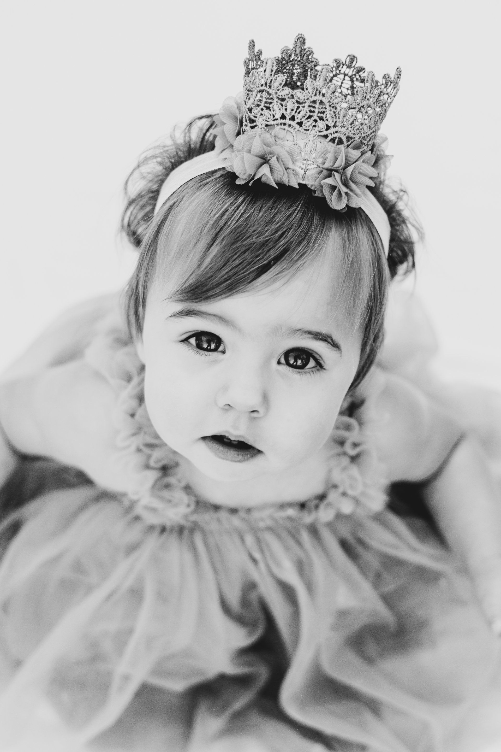 A black and white photo of a baby girl wearing a crown.