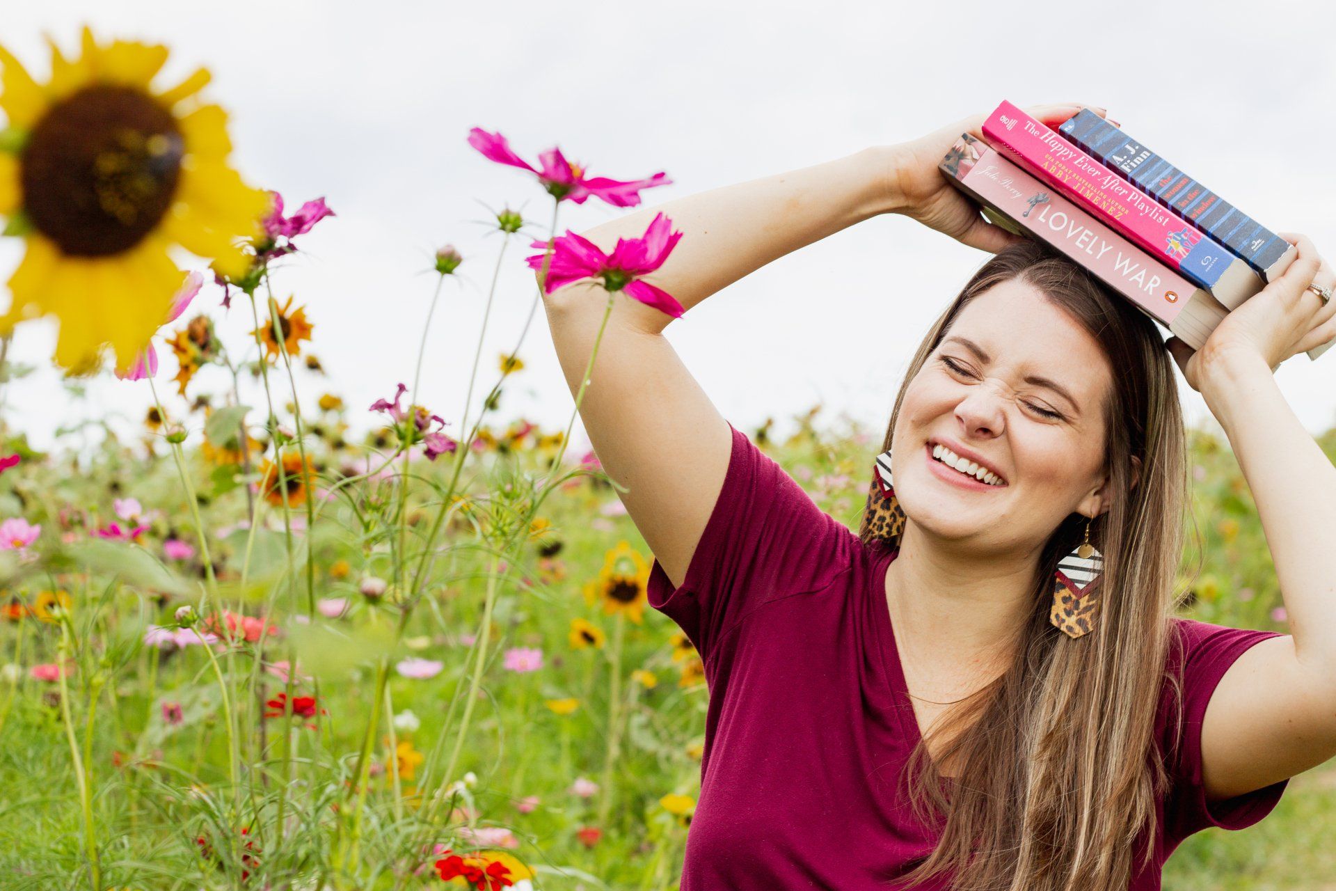 A woman is holding a stack of books on her head in a field of flowers.
