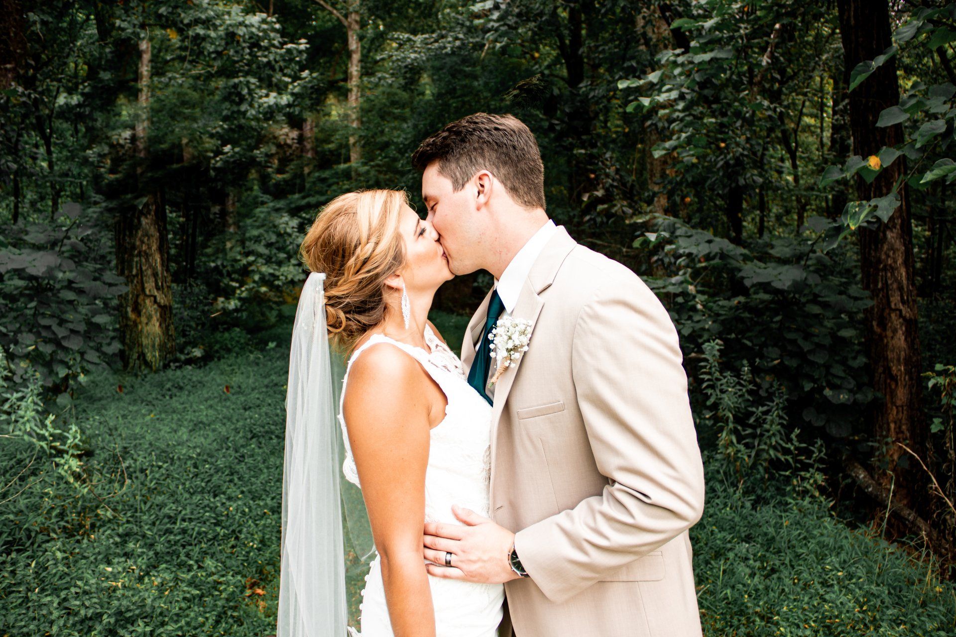 A bride and groom are kissing in the woods.
