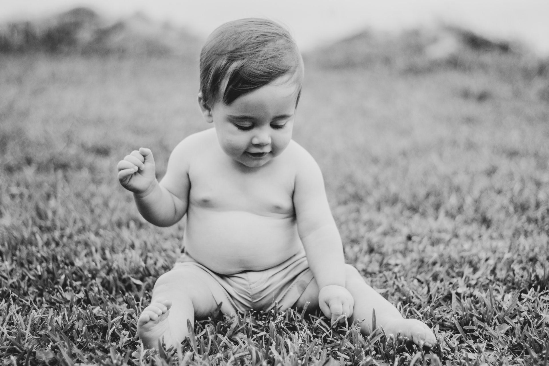 A baby is sitting in the grass in a black and white photo.