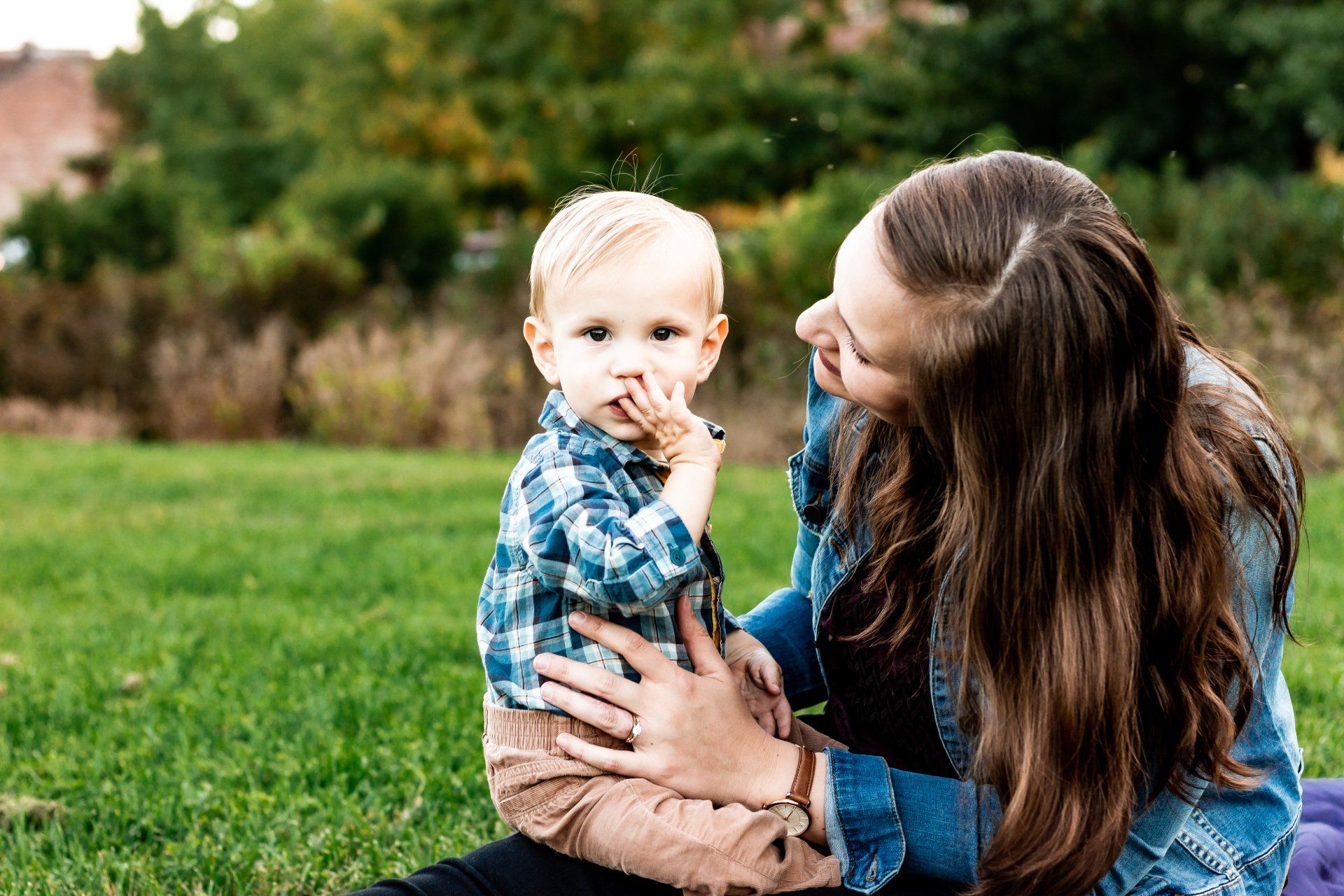 A woman is sitting on the grass holding a baby.