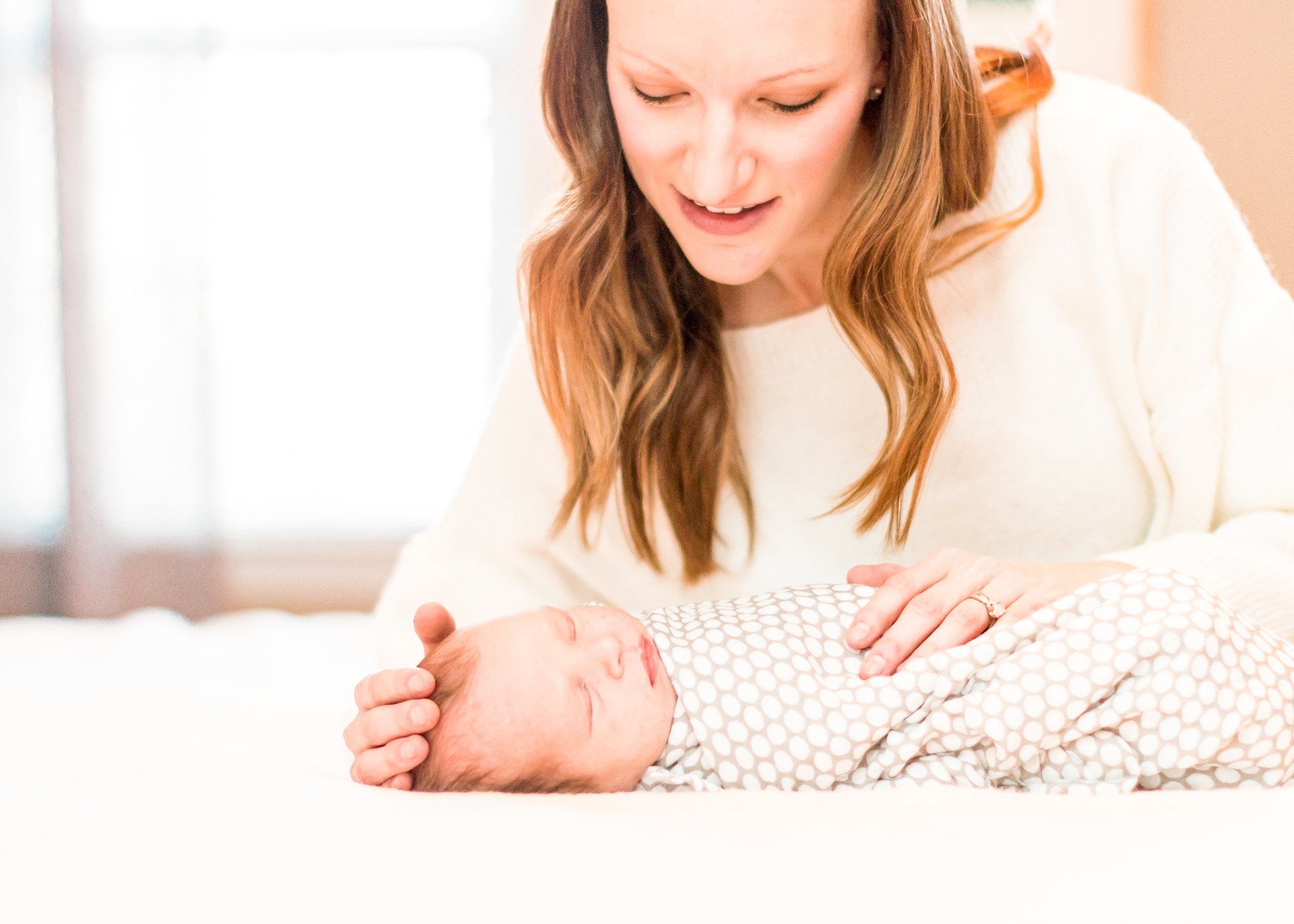 A woman is holding a newborn baby wrapped in a blanket on a bed.