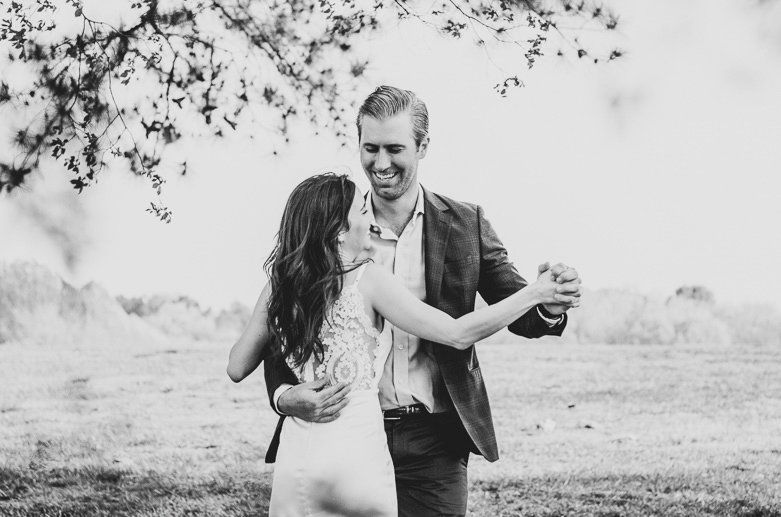 A black and white photo of a bride and groom dancing in a field.