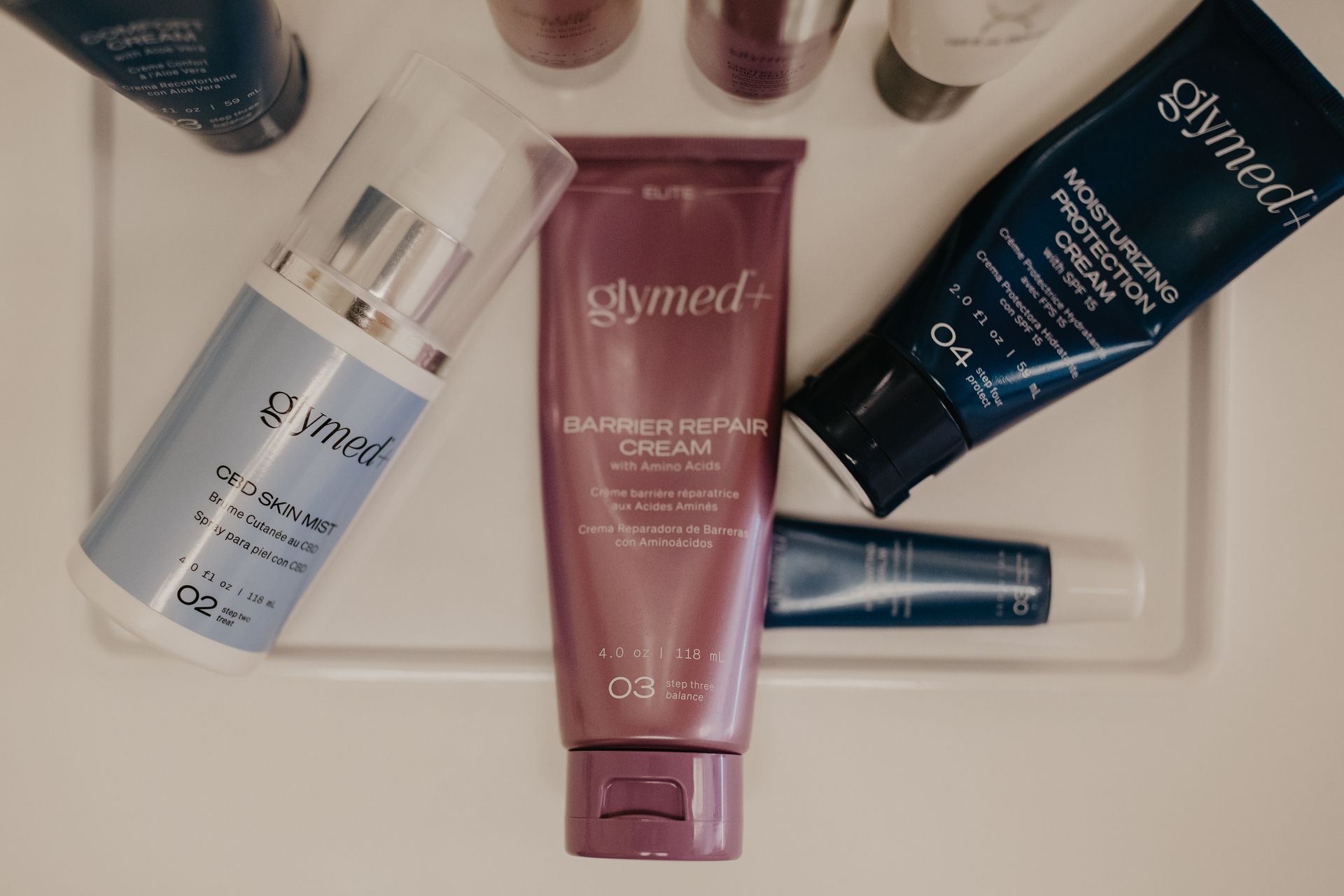 A bottle of glymed cream is surrounded by other bottles