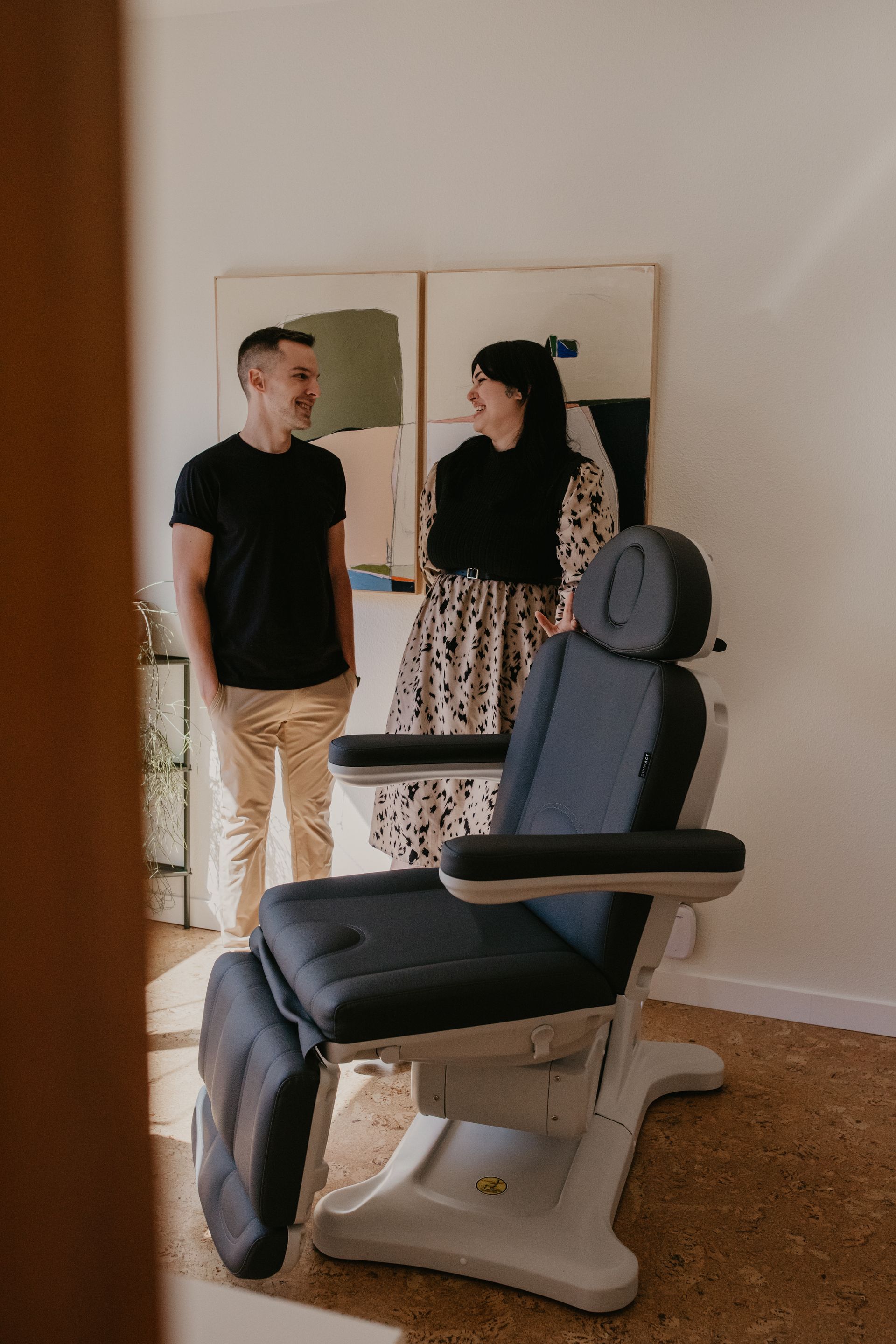 A man and a woman are standing next to a chair in a room.