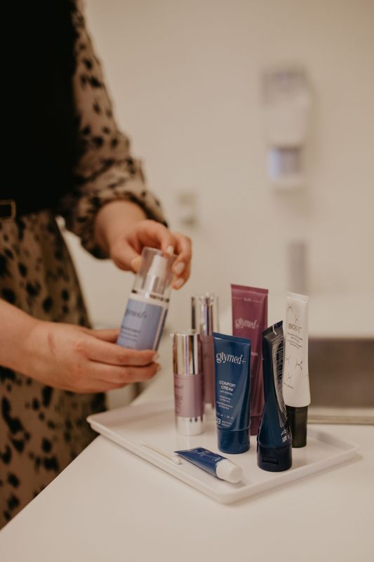 A woman is holding a bottle of lotion next to a tray of cosmetics.