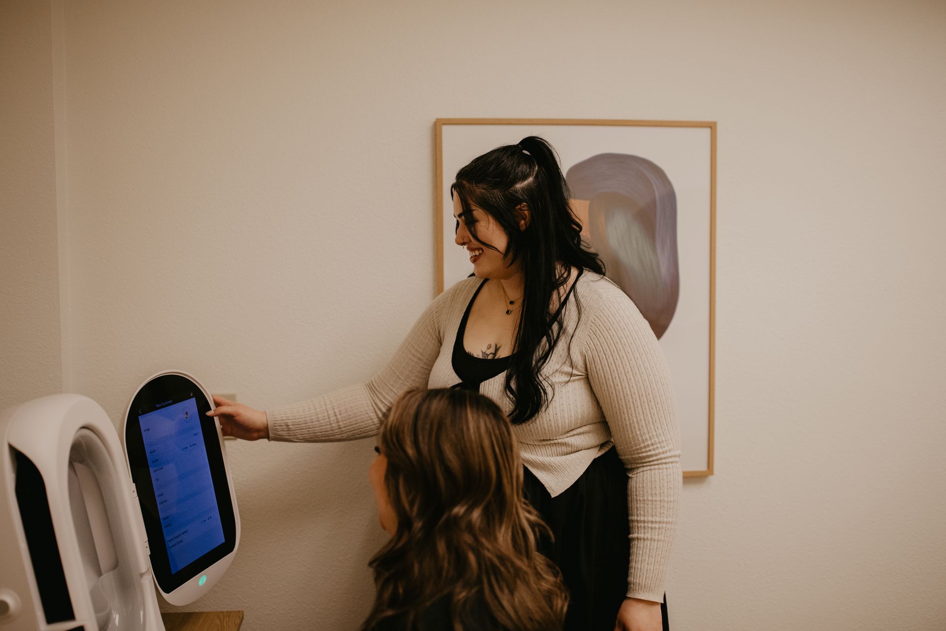 Two people at a professional skincare consultation, one adjusting settings on a digital skin analysis device.