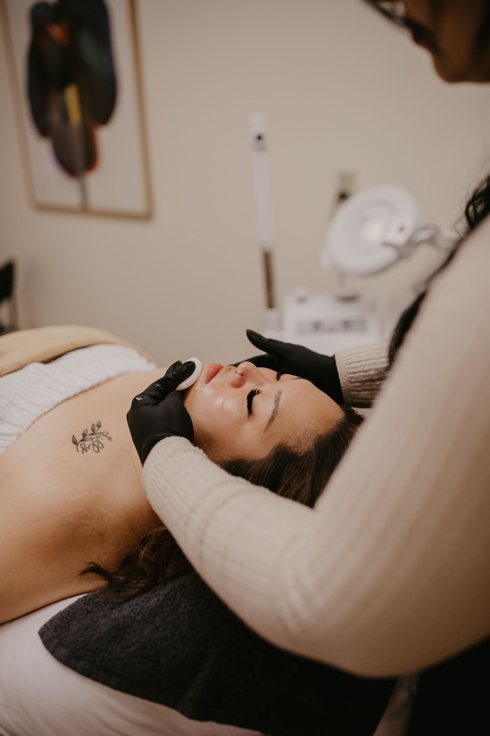 A professional in black gloves uses a cotton pad to cleanse a client’s face during a spa treatment.