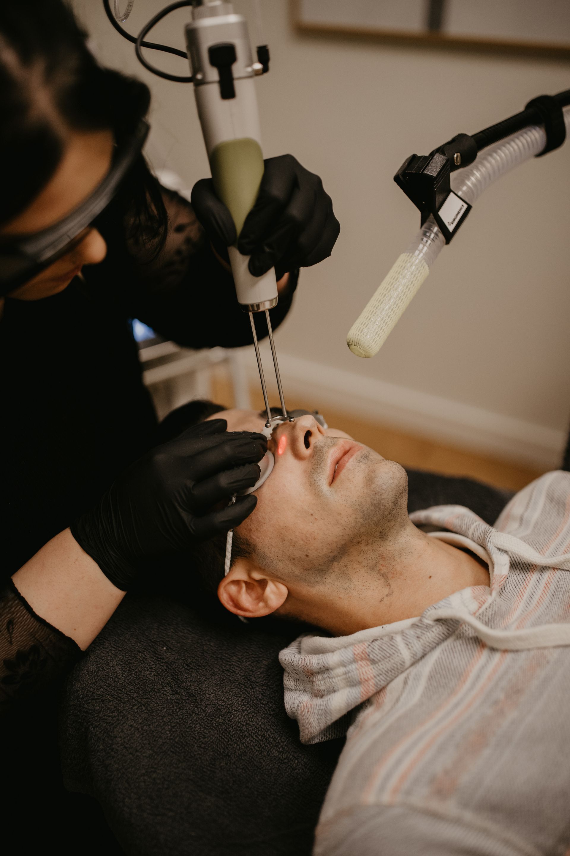 Person receiving laser treatment on face; medical professional holding device.