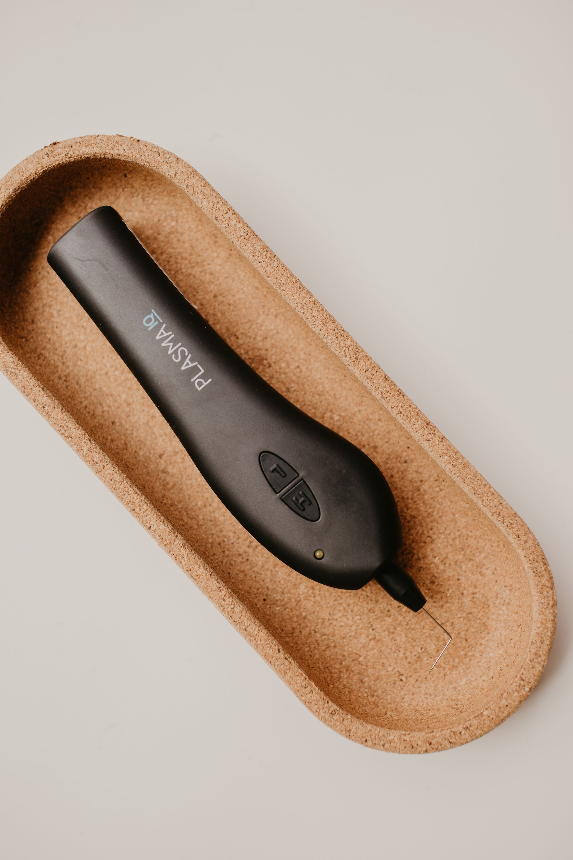 Black Plasma pen in a brown cork tray on a gray surface.