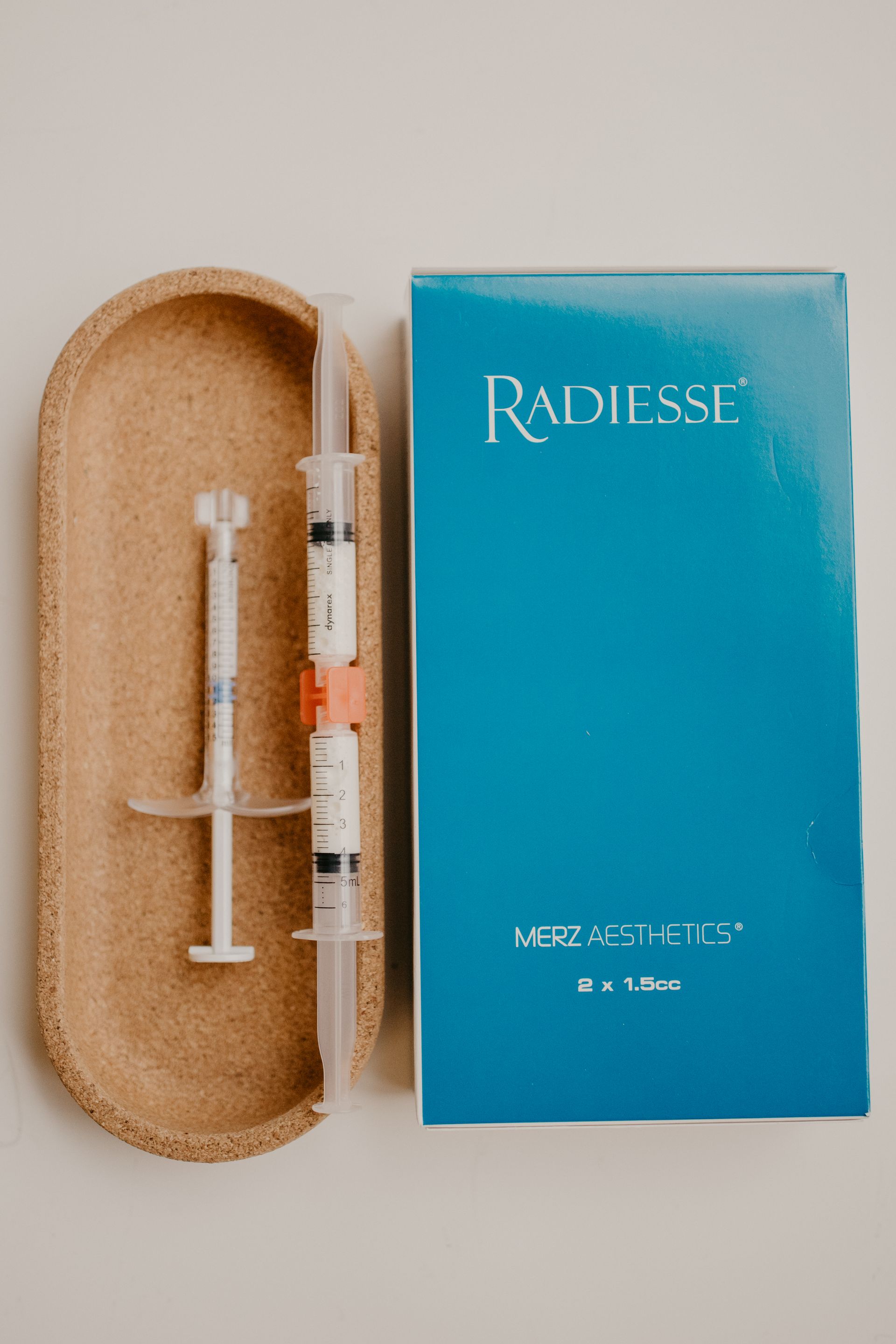 Radiesse dermal filler packaging with two syringes on a cork tray, blue box.