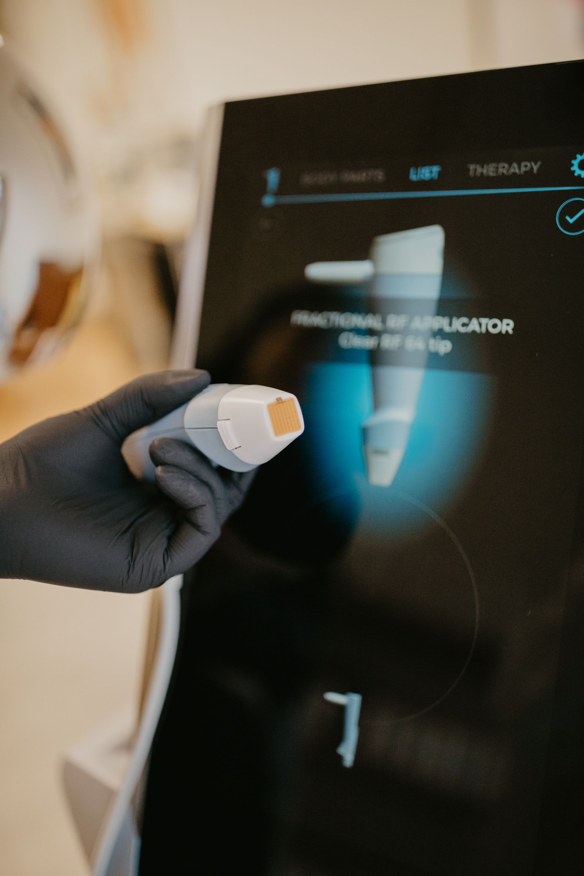 Hand holding a fractional RF applicator near a touchscreen display.