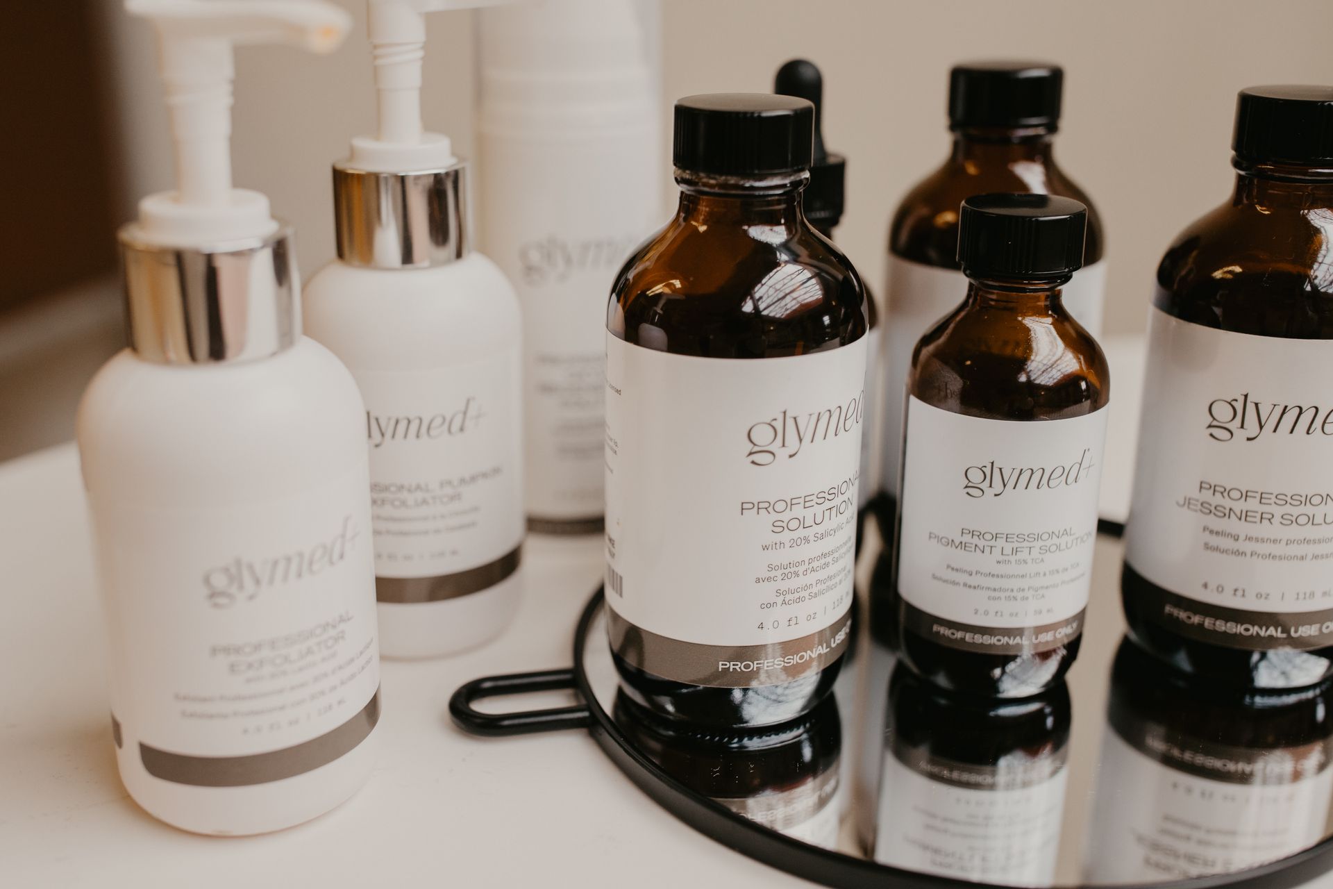 Several white and amber bottles of GlyMed Plus professional skincare products arranged on a surface.